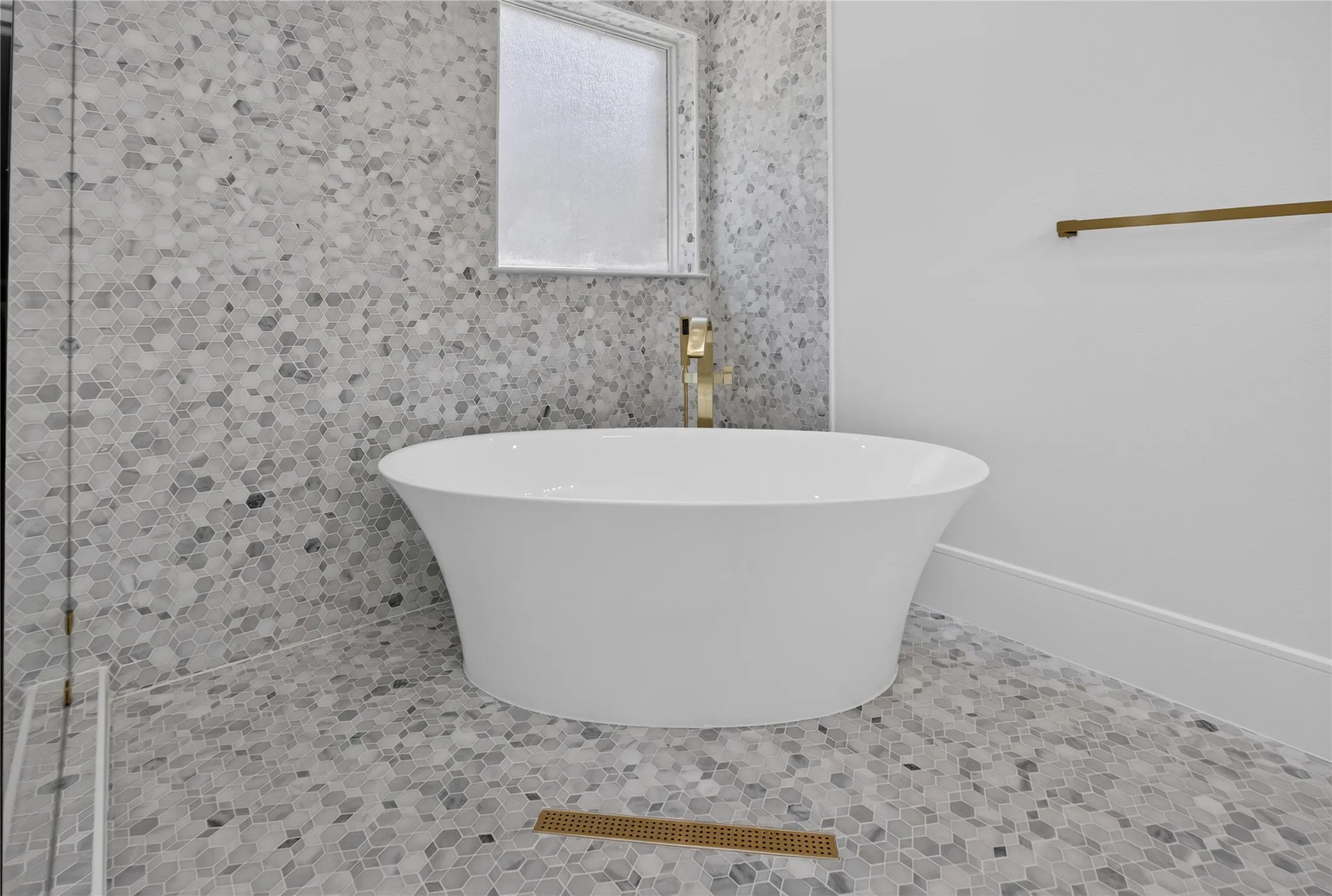 Freestanding soaking tub set against a mosaic tiled wall and flooring