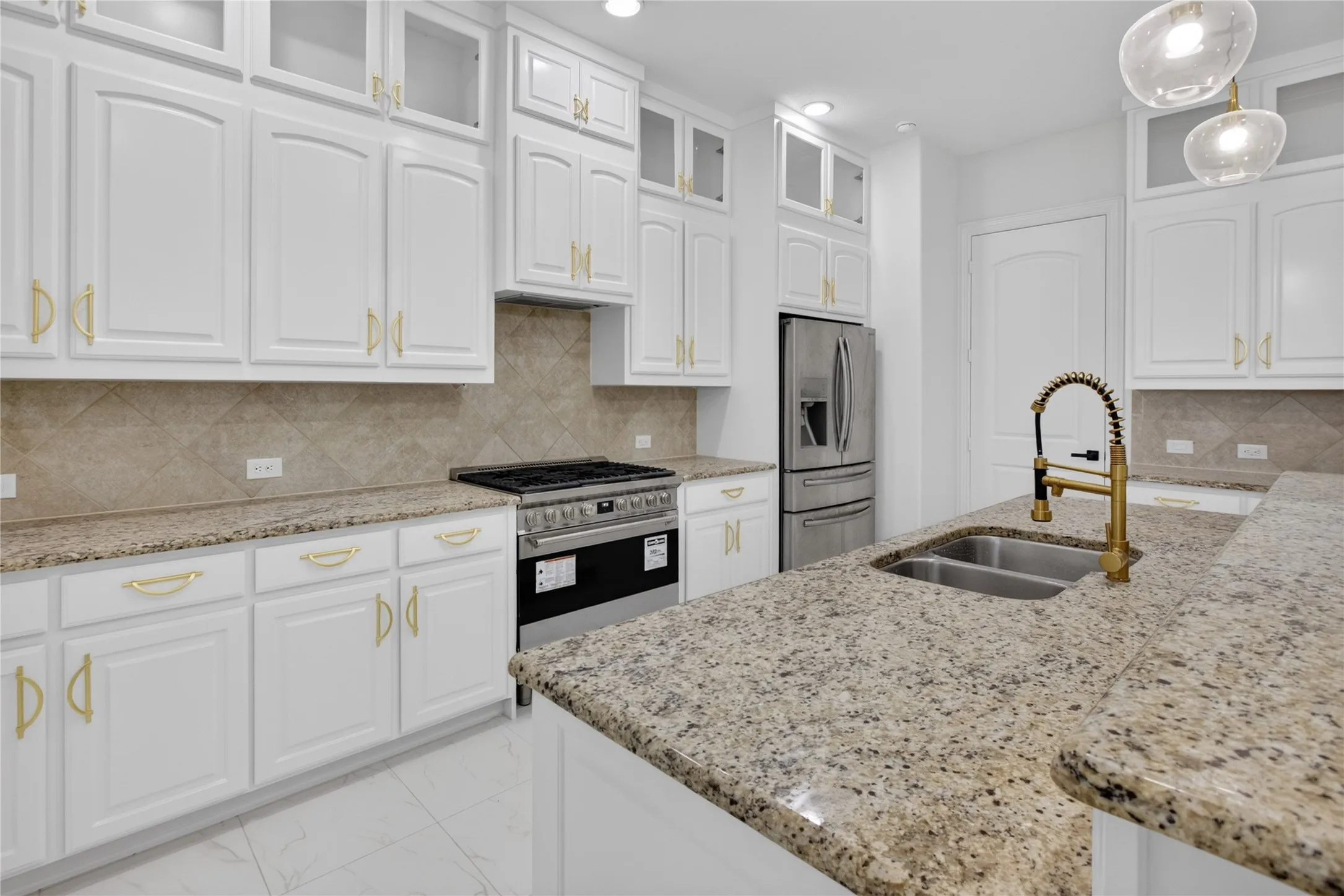 Modern kitchen featuring white cabinetry with gold-finish hardware, stainless steel appliances, and a gas range