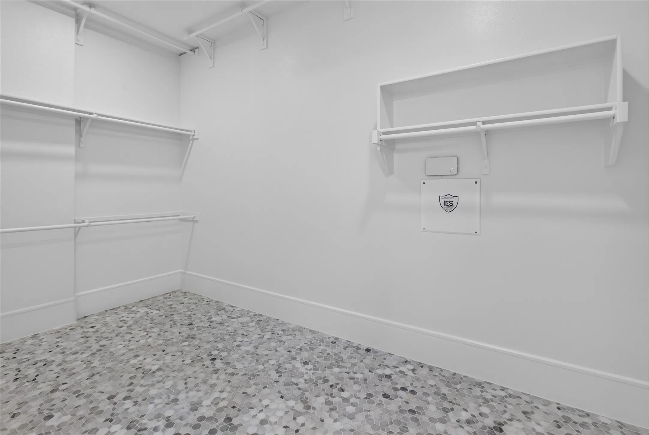 Walk-in closet featuring multi-level hanging rods, upper shelving, white walls, white baseboards, and a mosaic tile floor