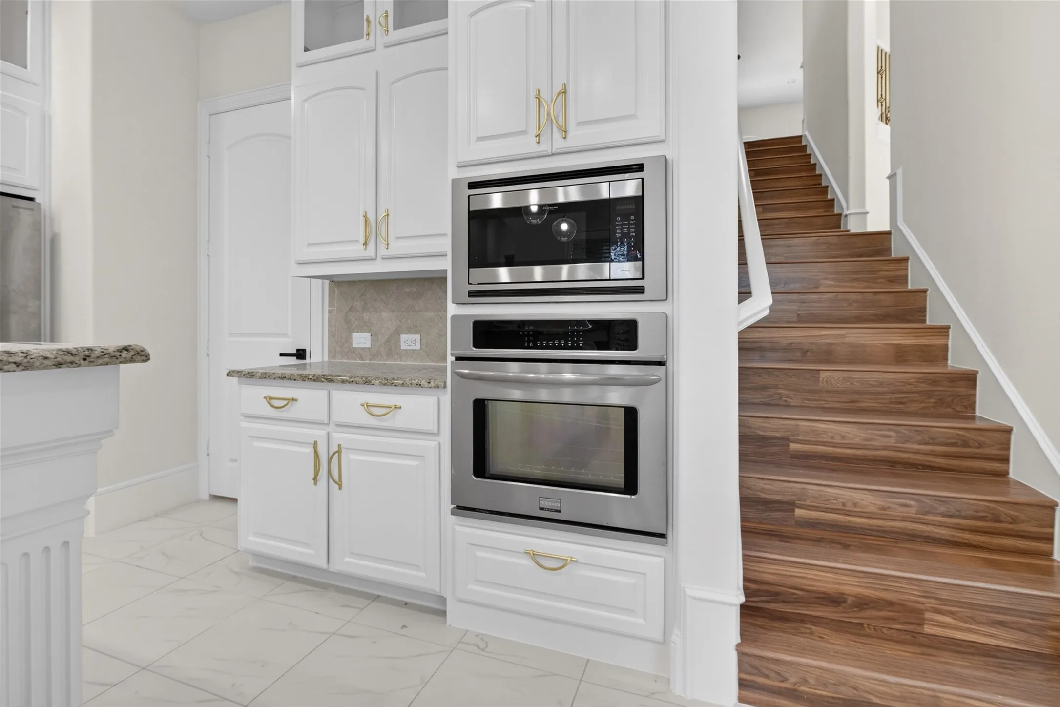 Kitchen featuring white cabinetry with gold-toned hardware, stone countertops, and a built-in stainless steel microwave and oven