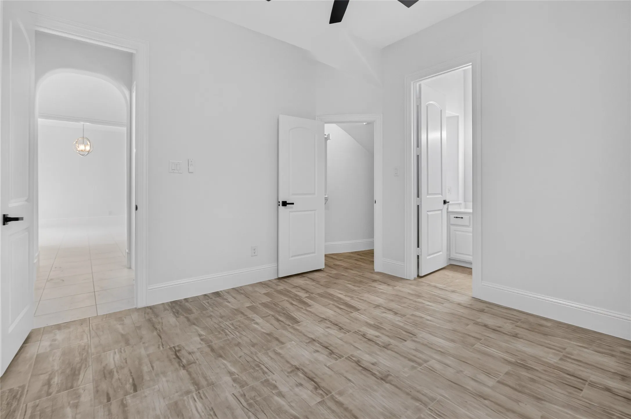 Spacious room featuring wood-finish flooring, white walls, and a ceiling fan