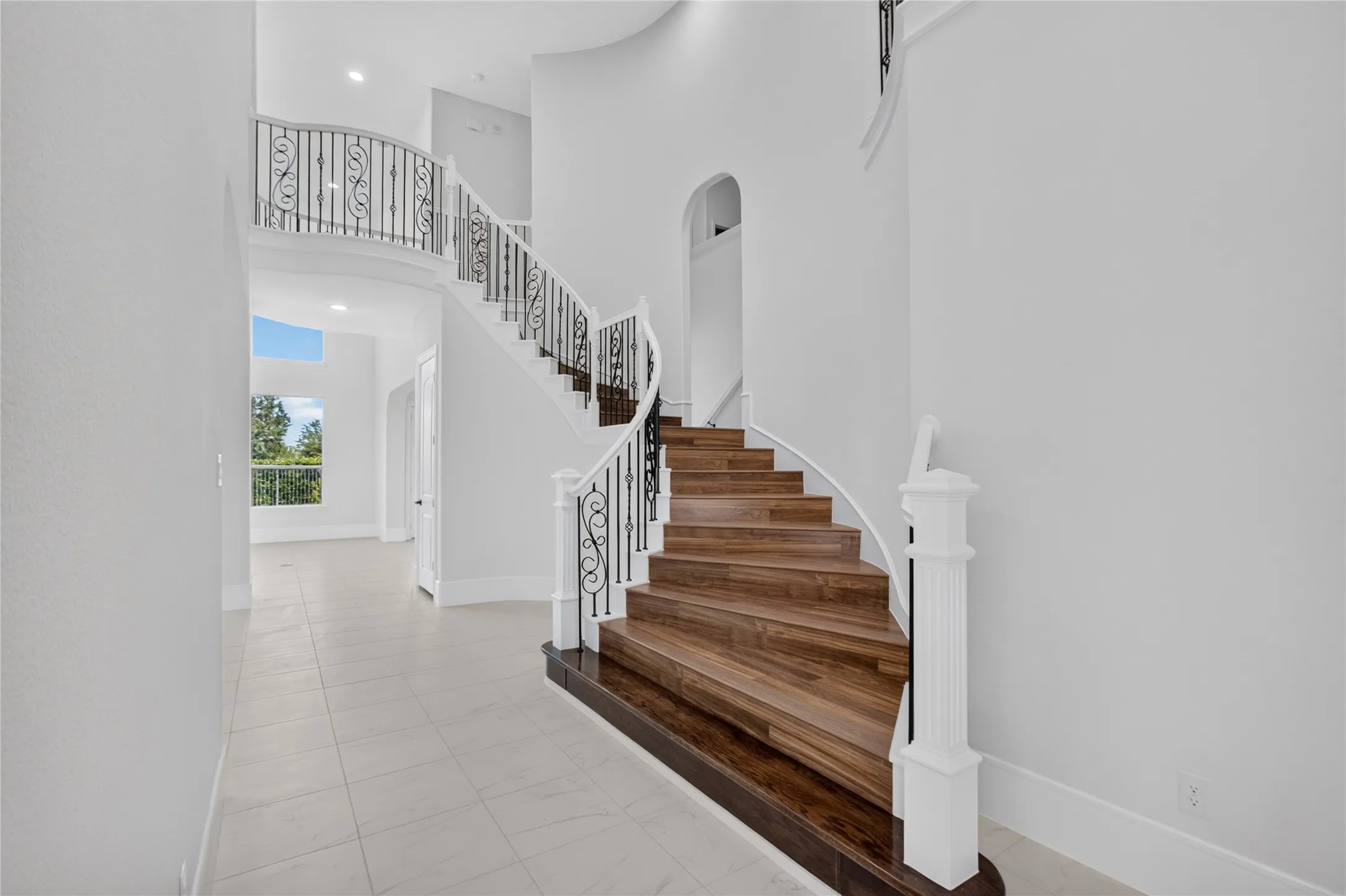 Grand curved staircase featuring wood-finish treads and risers, white balusters, and ornate black iron railings