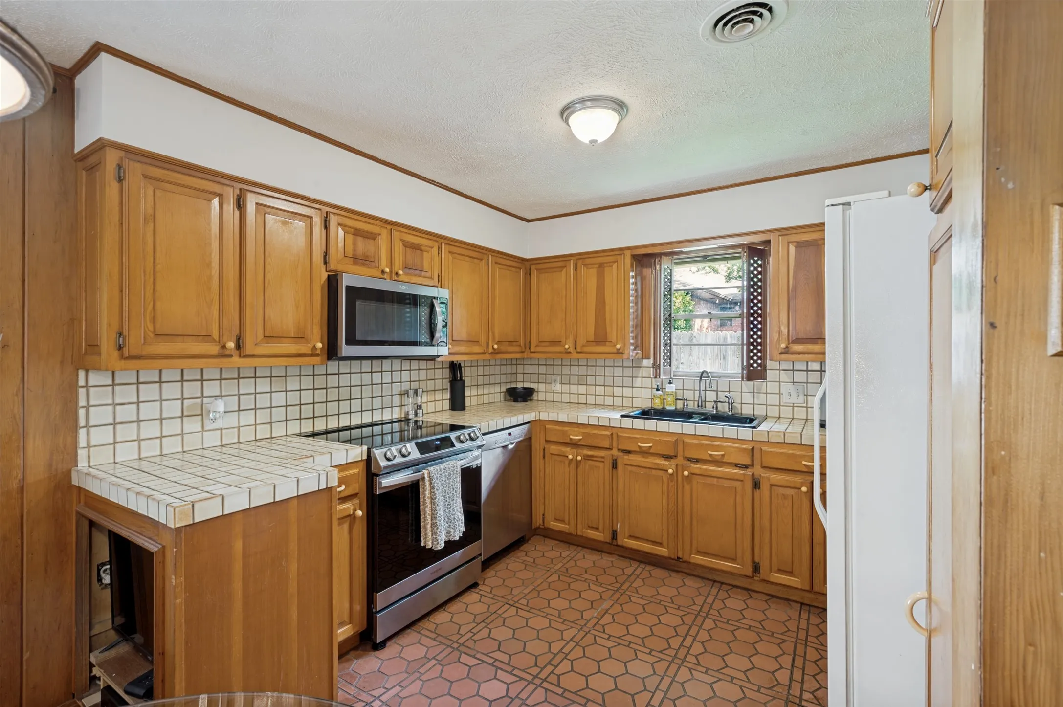 The kitchen features traditional honey-oak cabinets and tile countertops with the modern conveniences of stainless-steel appliances.