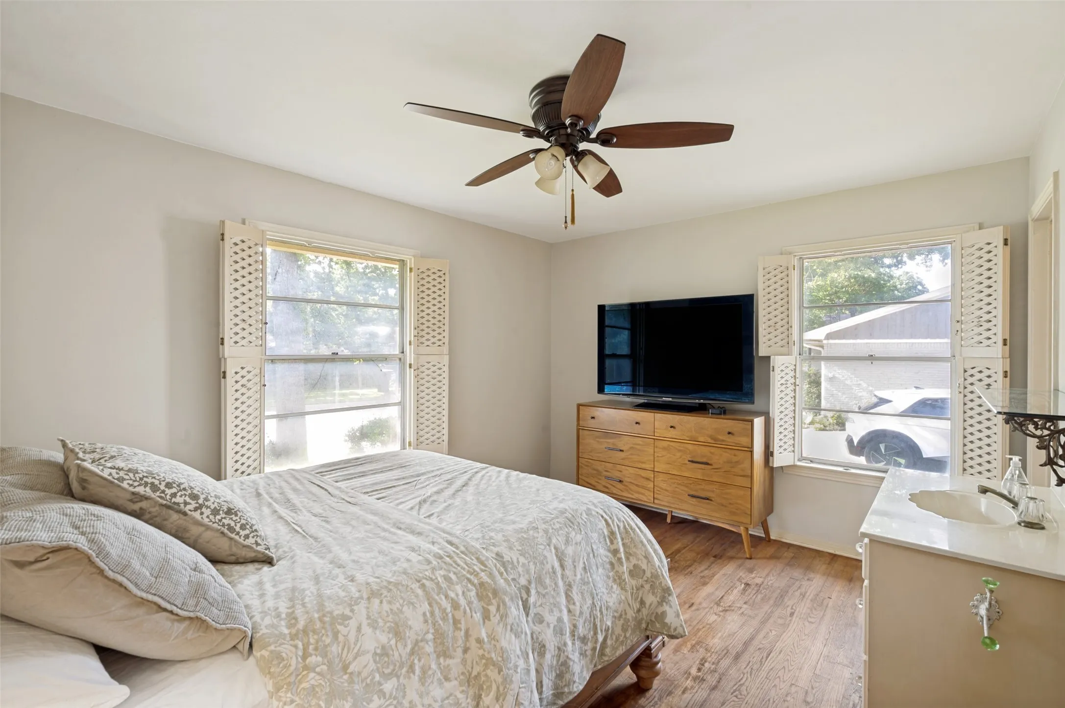 The primary bedroom features hardwood floors and large shuttered windows.
