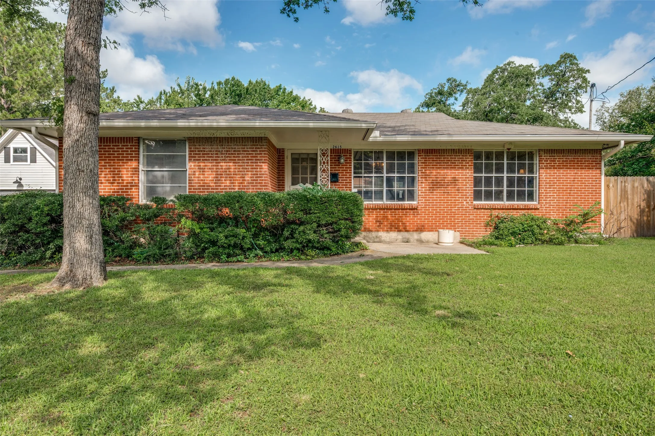 Charming single-story brick home nestled beneath mature shade trees offering timeless curb appeal.