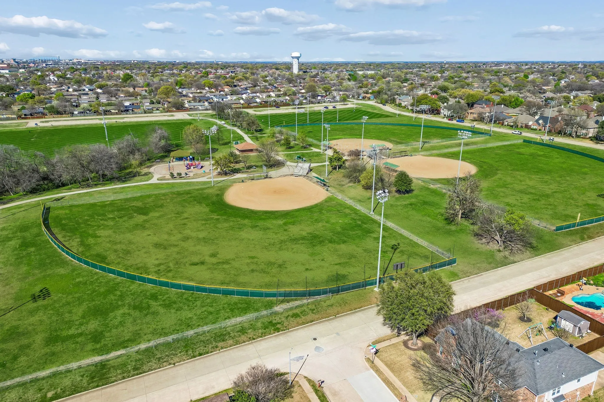 Expansive park grounds featuring multiple baseball fields, a playground, and walking paths
