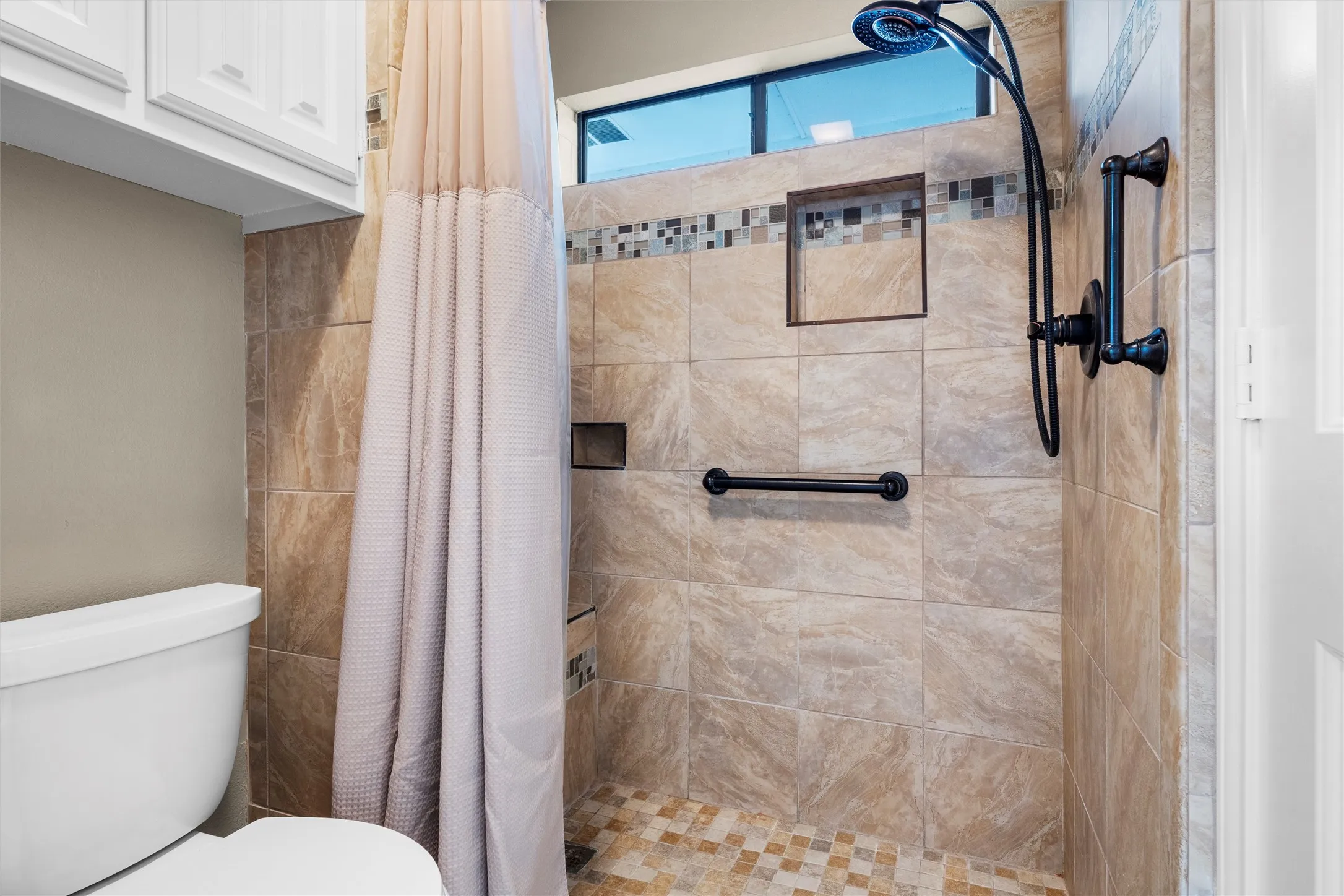 Tiled shower enclosure featuring a mosaic accent band, two built-in storage niches, and a handheld shower fixture