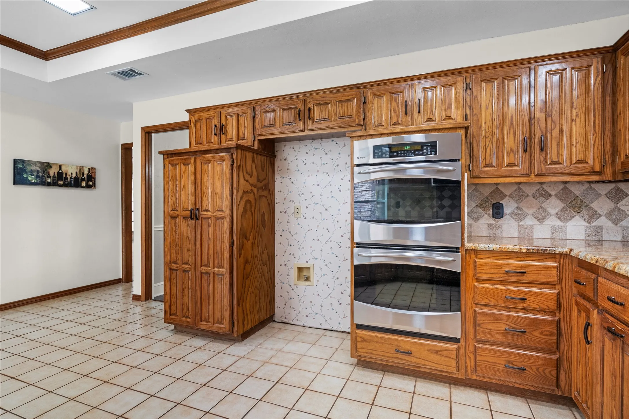 Kitchen featuring stainless steel double ovens, wood cabinetry, granite-style countertops, and a tiled backsplash
