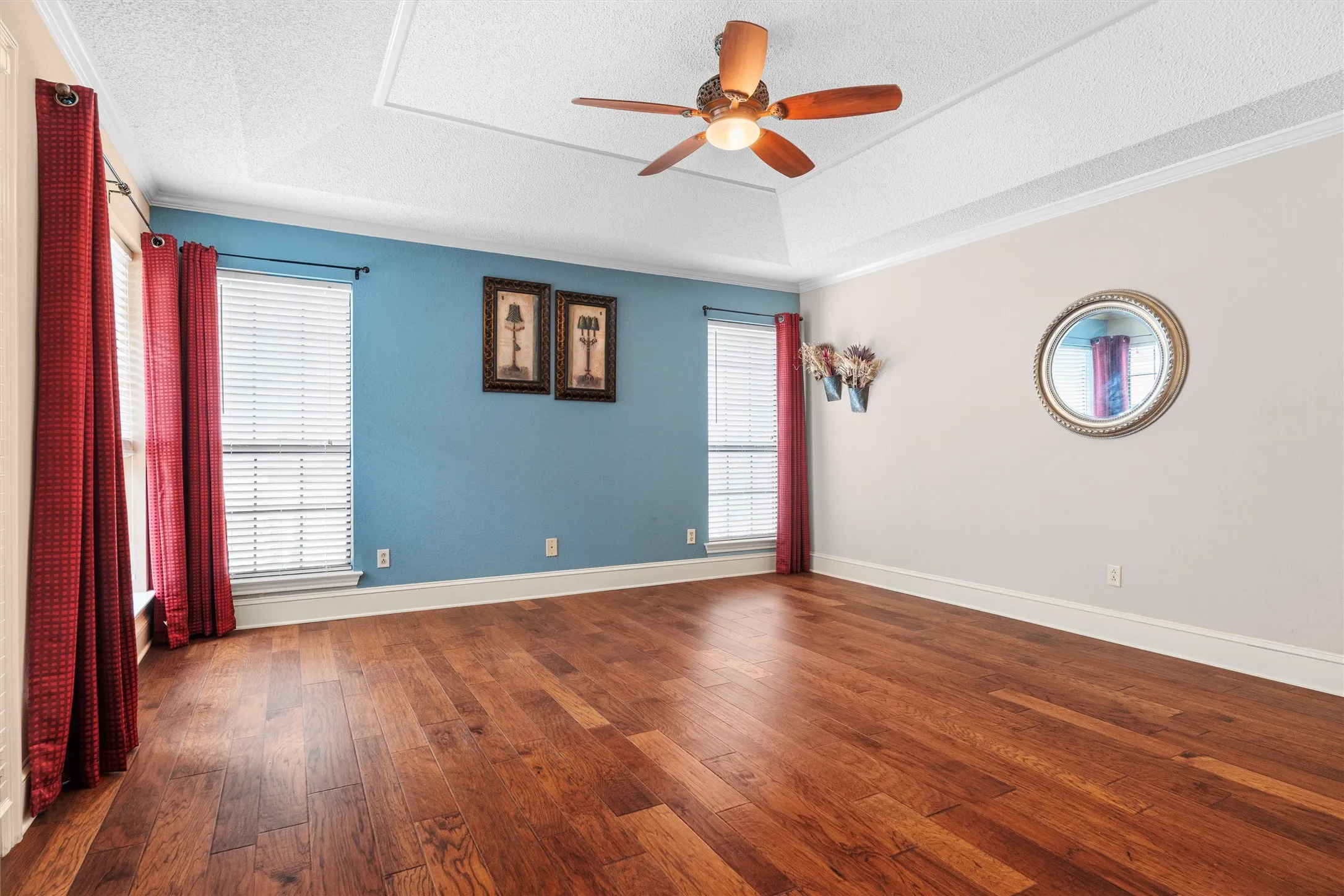 Spacious room featuring wood-finish flooring, a tray ceiling, and a ceiling fan