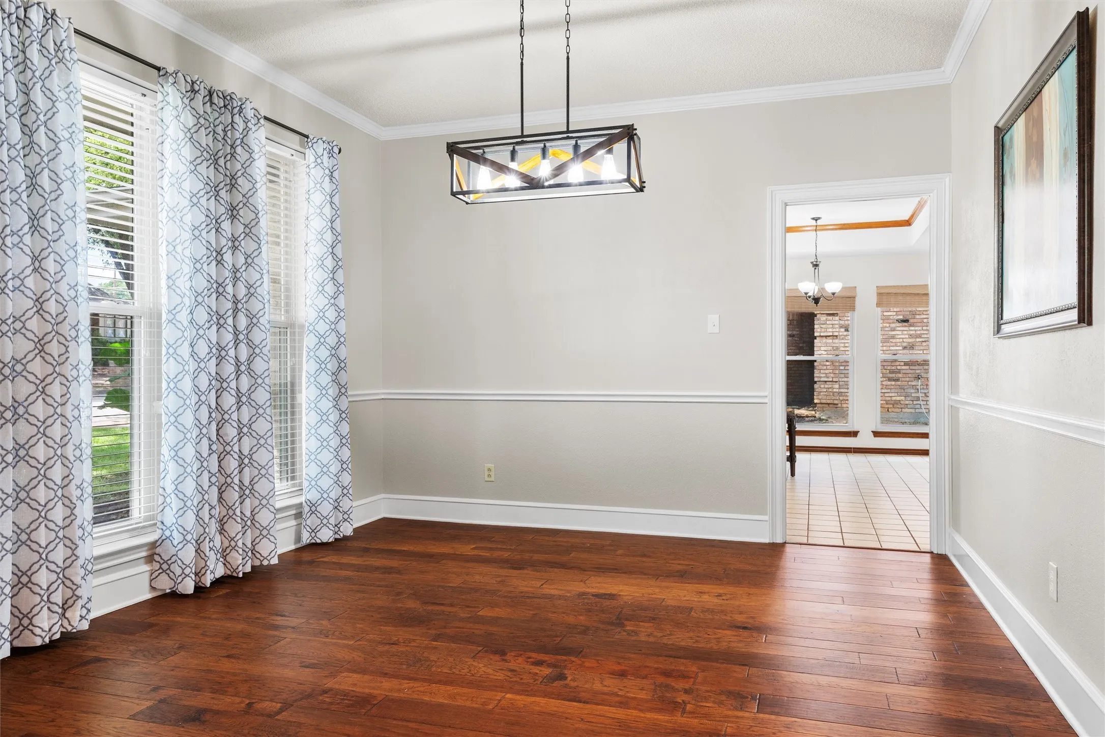 Spacious room featuring rich wood-finish flooring, crisp white trim, and a modern rectangular chandelier