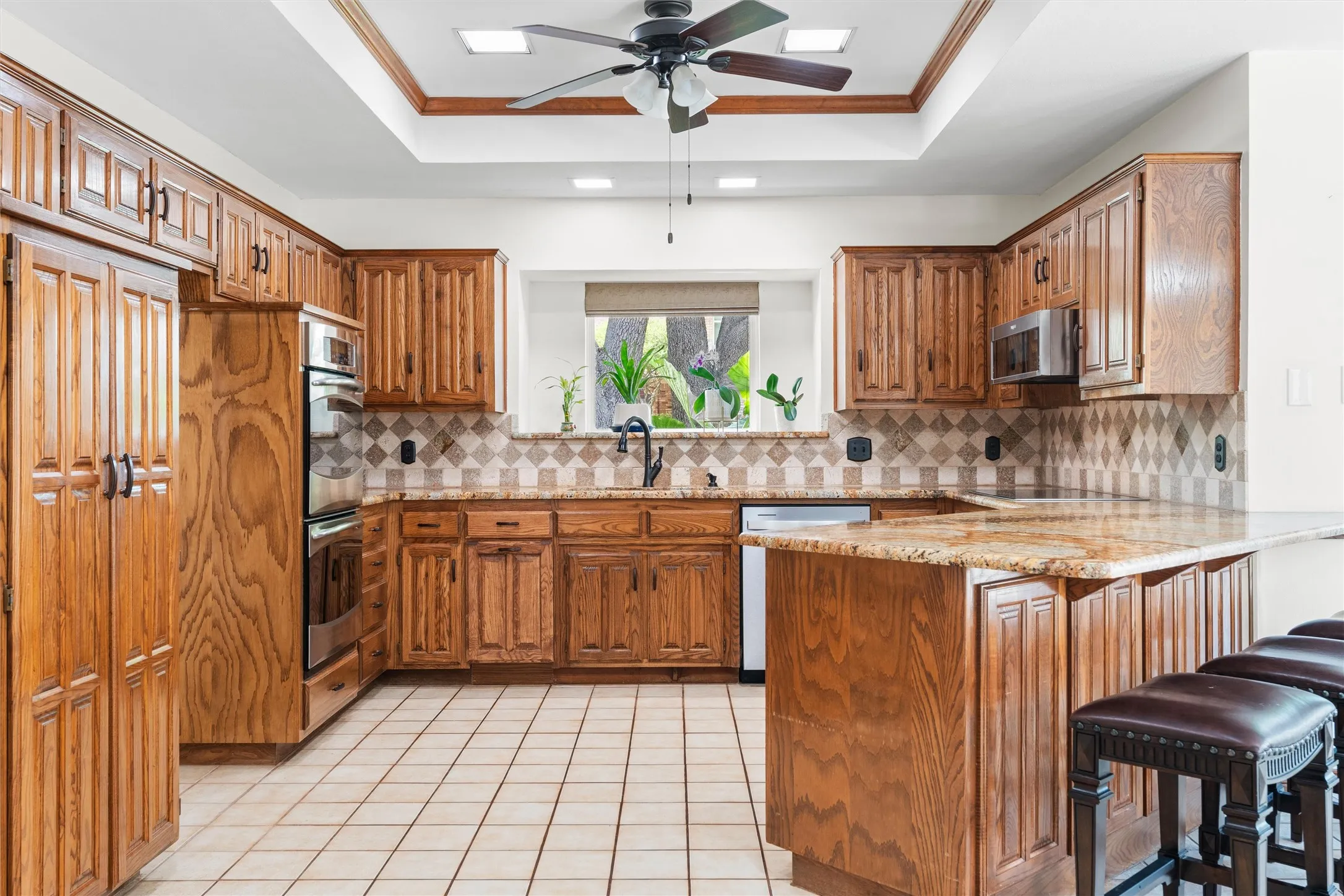 Spacious kitchen featuring extensive wood cabinetry, light-toned tile flooring, granite countertops, and a patterned tile backsplash