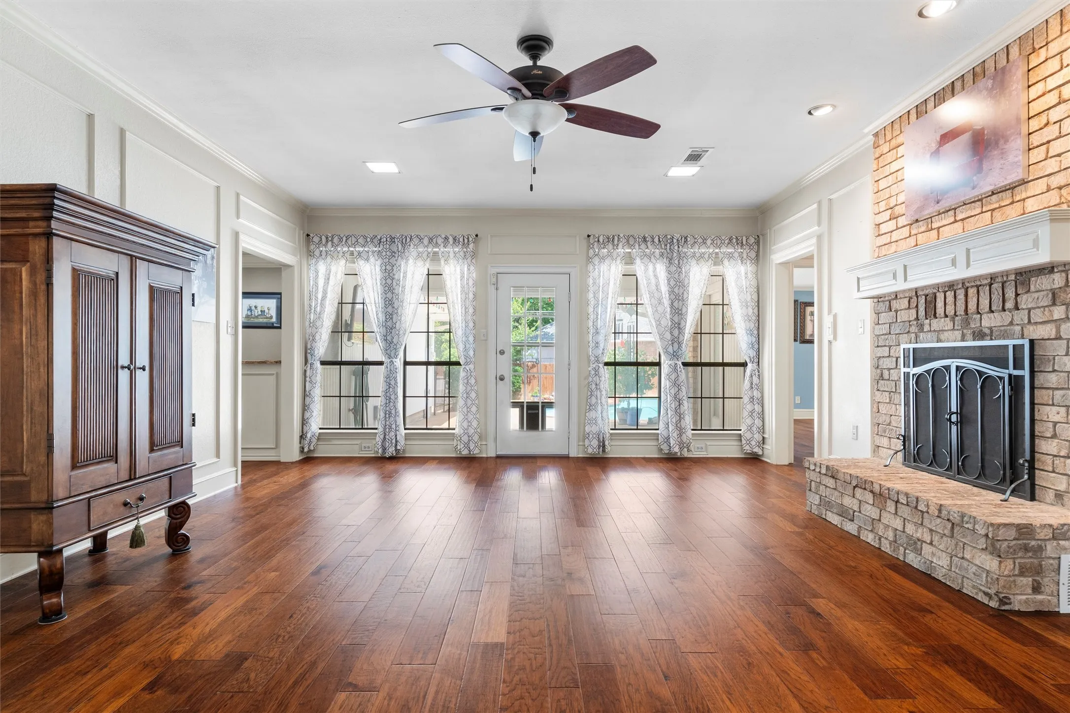 Spacious interior featuring wood-finish flooring, a brick fireplace with a white mantel, and multiple windows