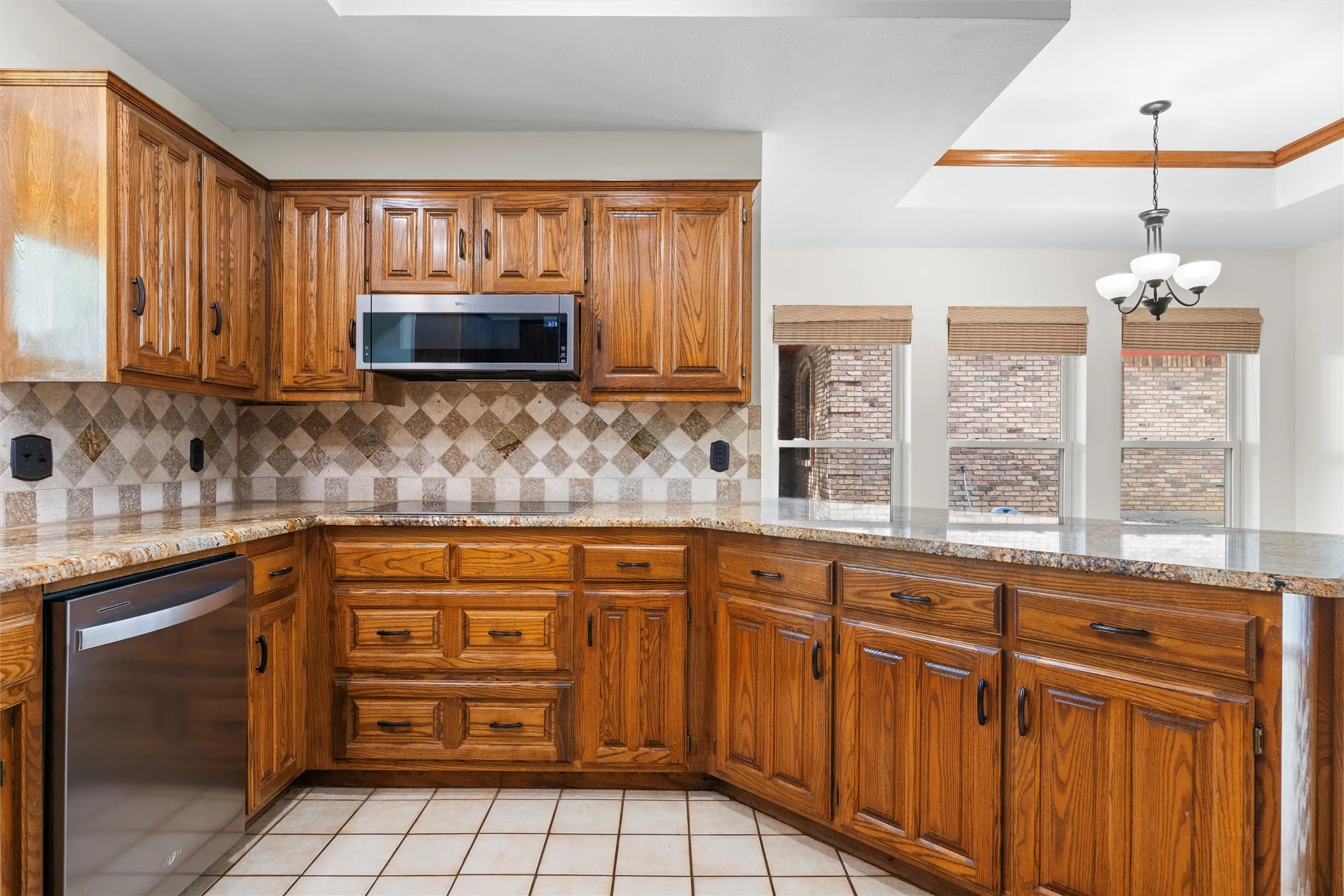 Corner kitchen featuring wood cabinetry, a stainless steel microwave, a built-in dishwasher, and a patterned tile backsplash