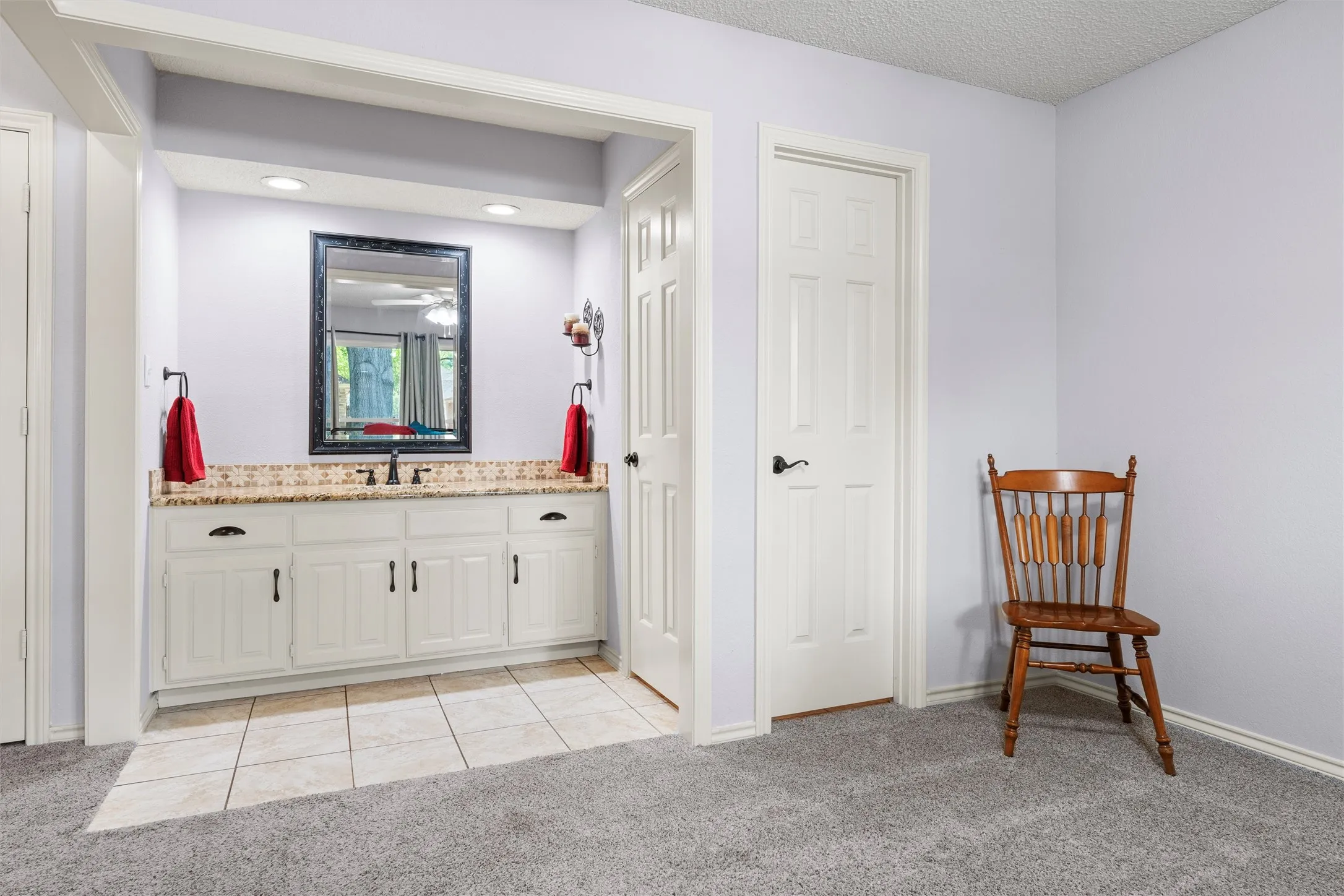 Built-in vanity with white cabinetry, a light-toned granite countertop, and a dark-framed mirror