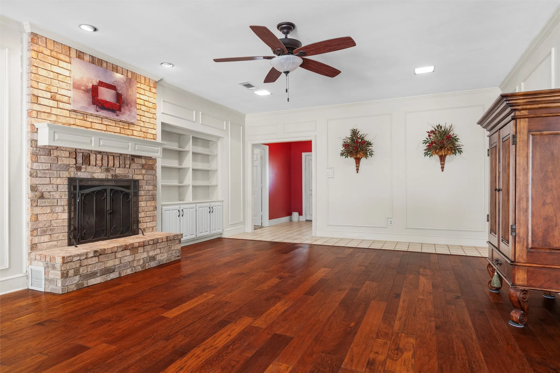 Spacious interior featuring wood-finish flooring, a brick fireplace with a white mantel, built-in shelving, recessed lighting, and a ceiling fan