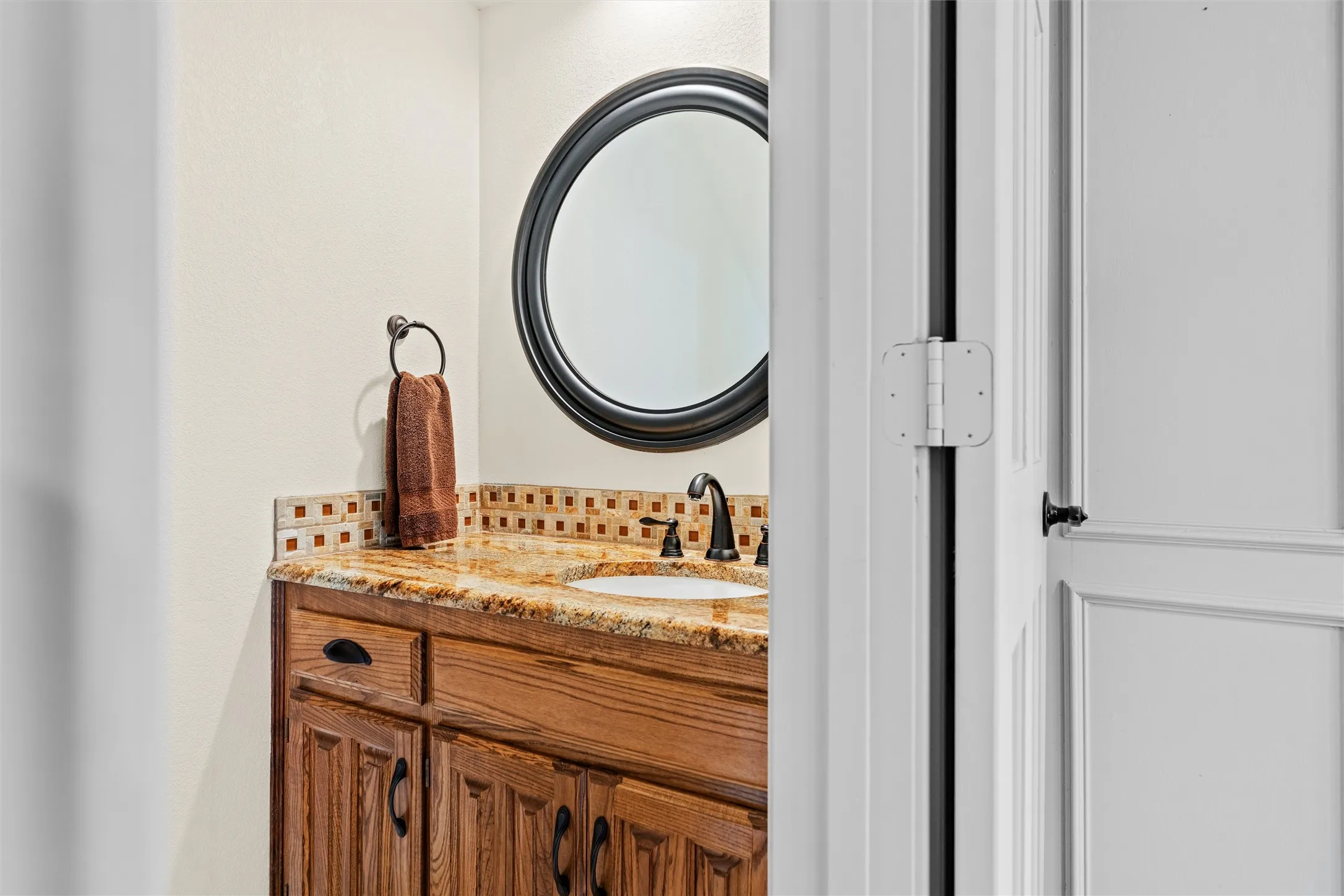 Bathroom vanity featuring a light-toned stone countertop, integrated sink, and square tile backsplash