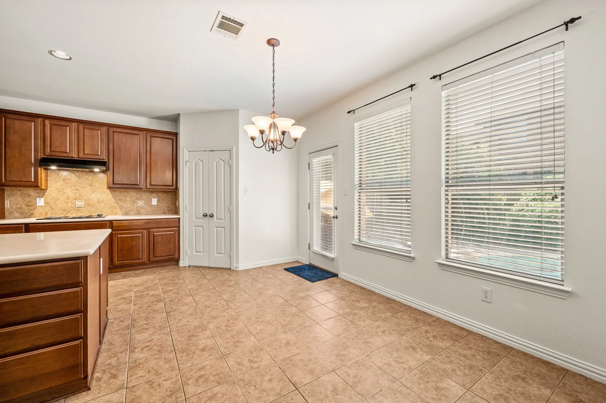 Open concept kitchen and dining area featuring wood cabinetry, stone-finish backsplash, built-in cooktop, and a kitchen island with stone-finish countertop