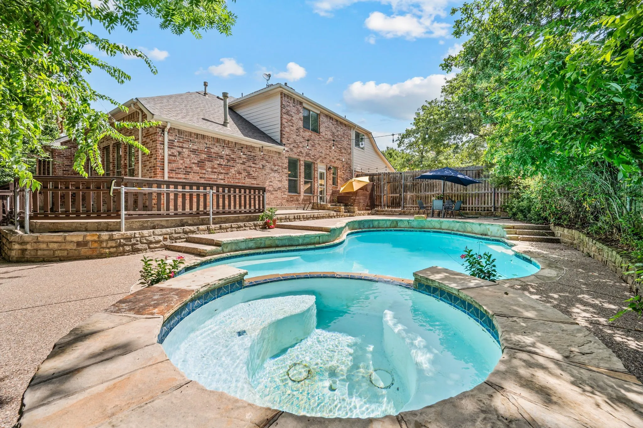 Spacious backyard featuring a multi-level pool with integrated spa, an expansive wood deck, and a surrounding stone paver patio