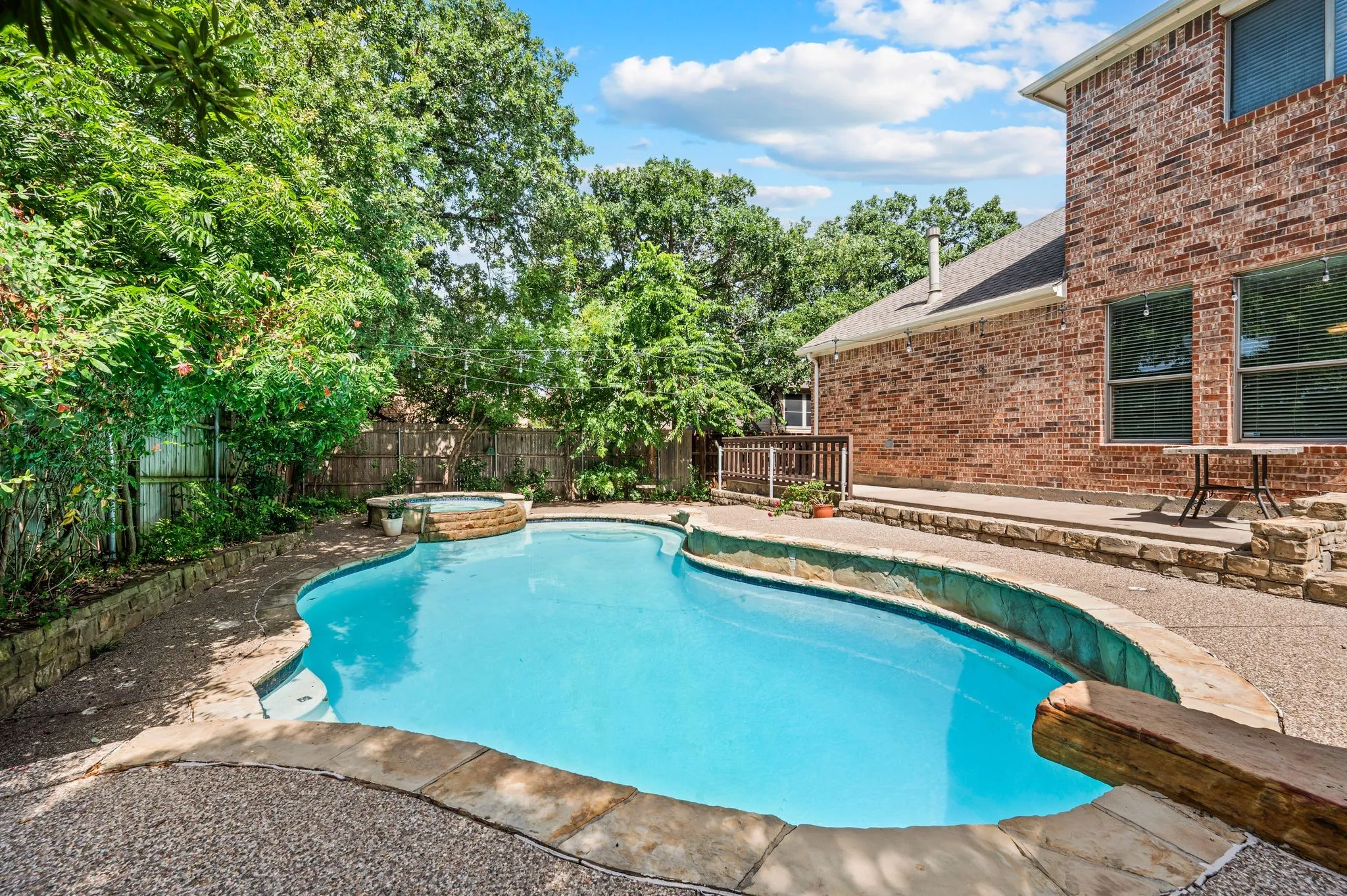 Inviting backyard featuring a freeform swimming pool with integrated spa, a stone coping perimeter, and a concrete patio