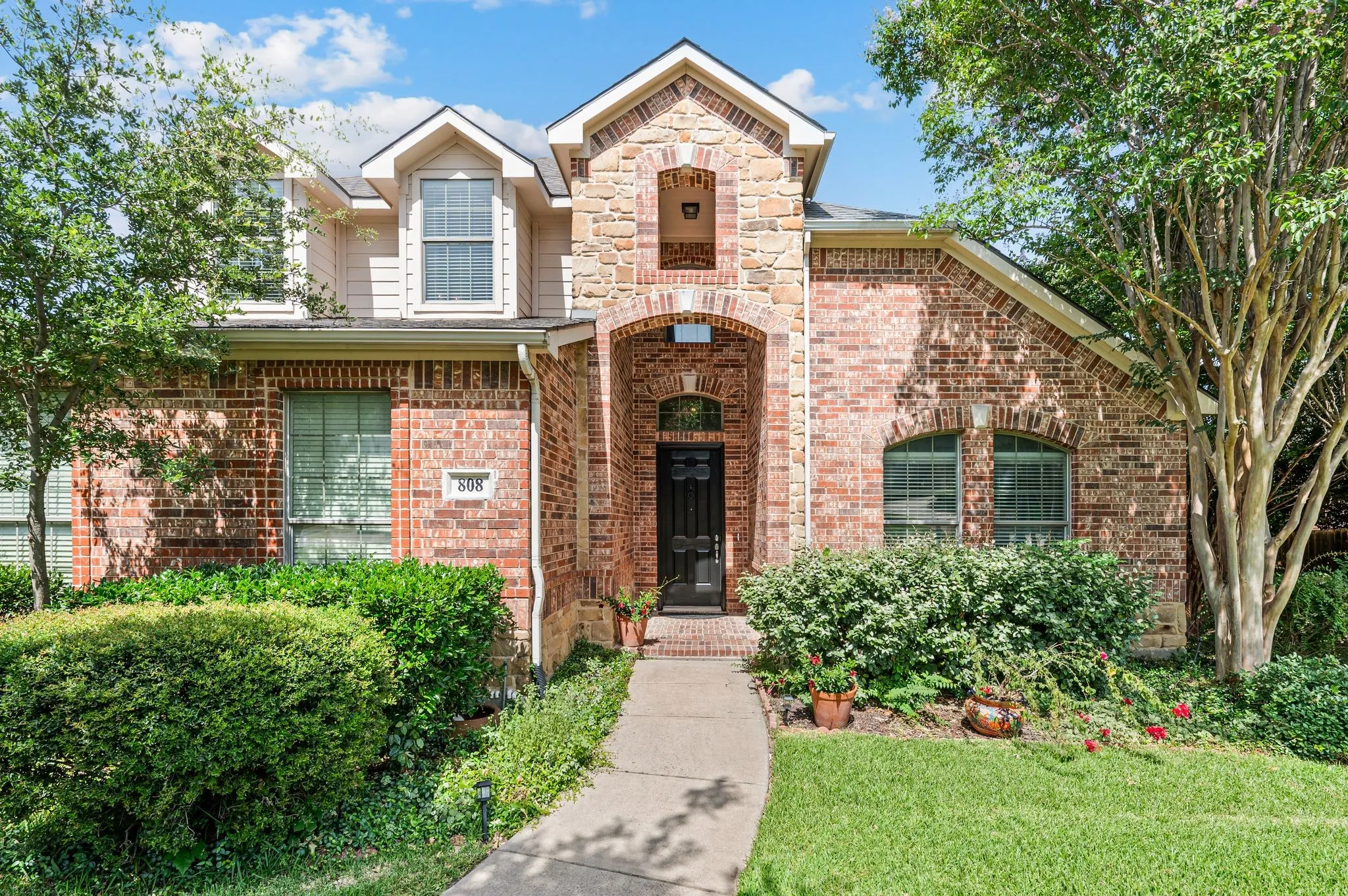 Brick and stone facade featuring an arched entry, multiple gables, and a concrete pathway