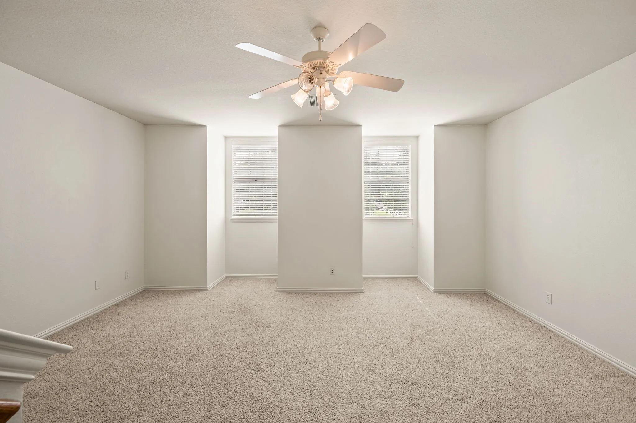 Brightly lit interior space featuring soft neutral carpeting, crisp white walls, and a ceiling fan with integrated lighting