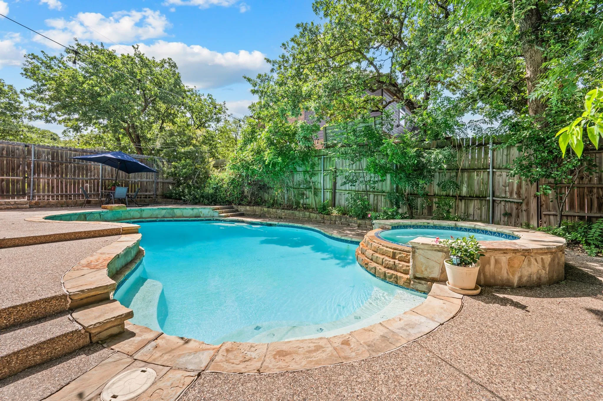 Outdoor living area featuring a freeform swimming pool, integrated spa with stone surround, and extensive concrete decking