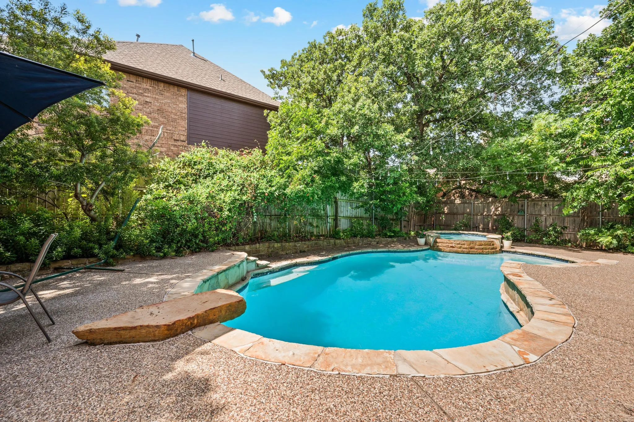 Freeform swimming pool with stone coping, an integrated spa, and expansive aggregate decking
