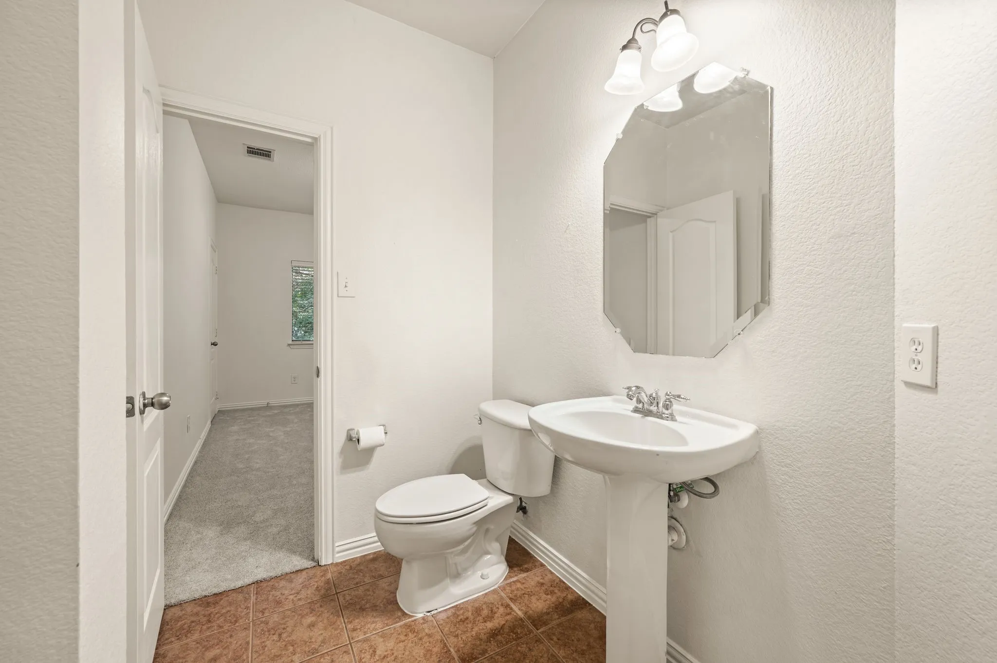 Pedestal sink with chrome faucet, octagonal mirror, and a two-light vanity fixture