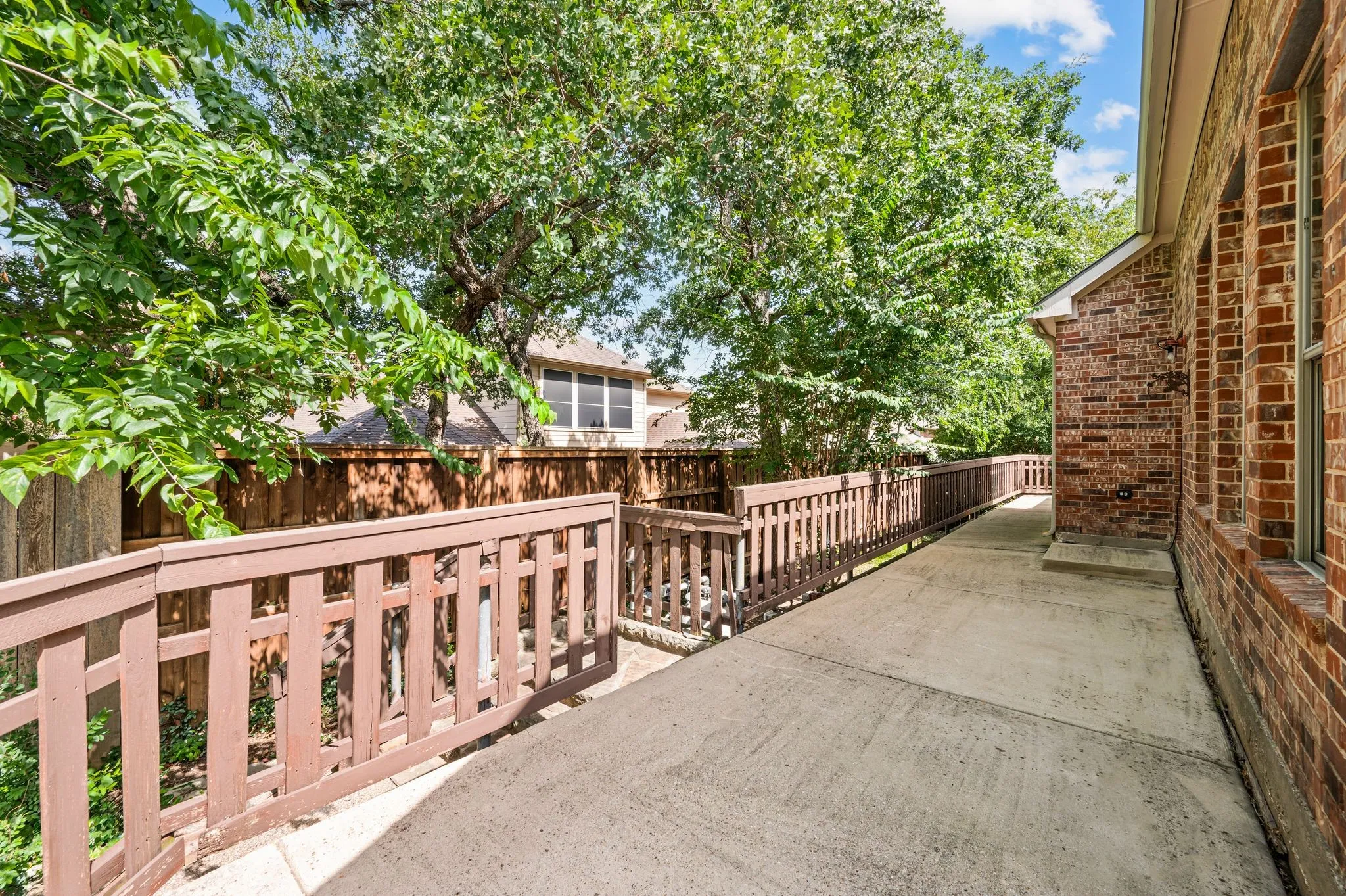 Exterior concrete walkway bordered by a wooden fence with wood railings