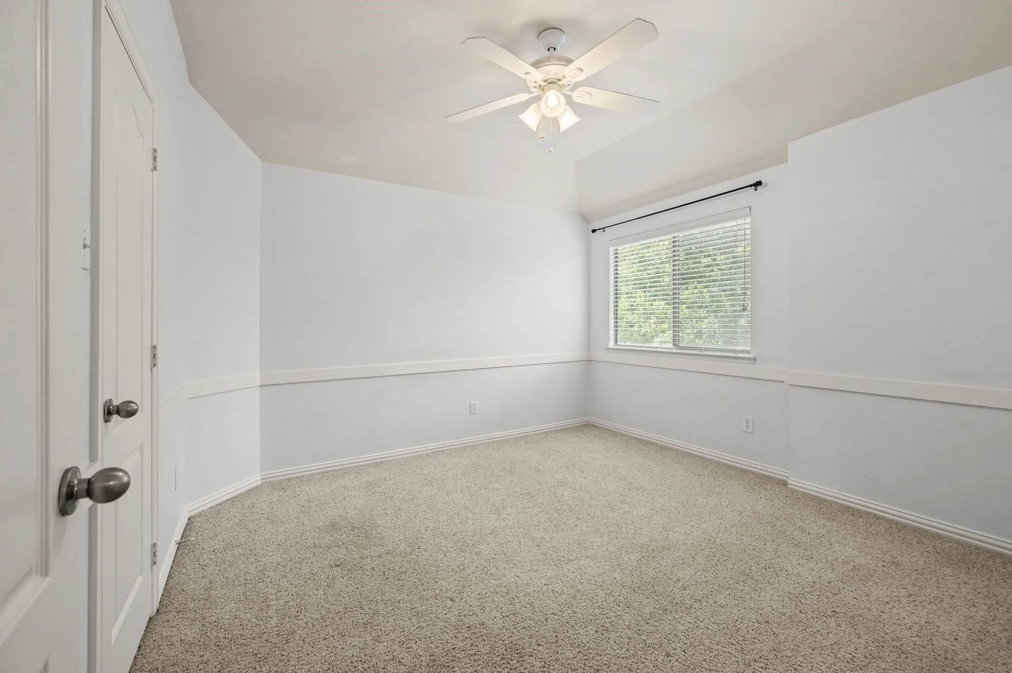 Carpeted room featuring a ceiling fan with light fixture, a window with blinds, and decorative wainscoting