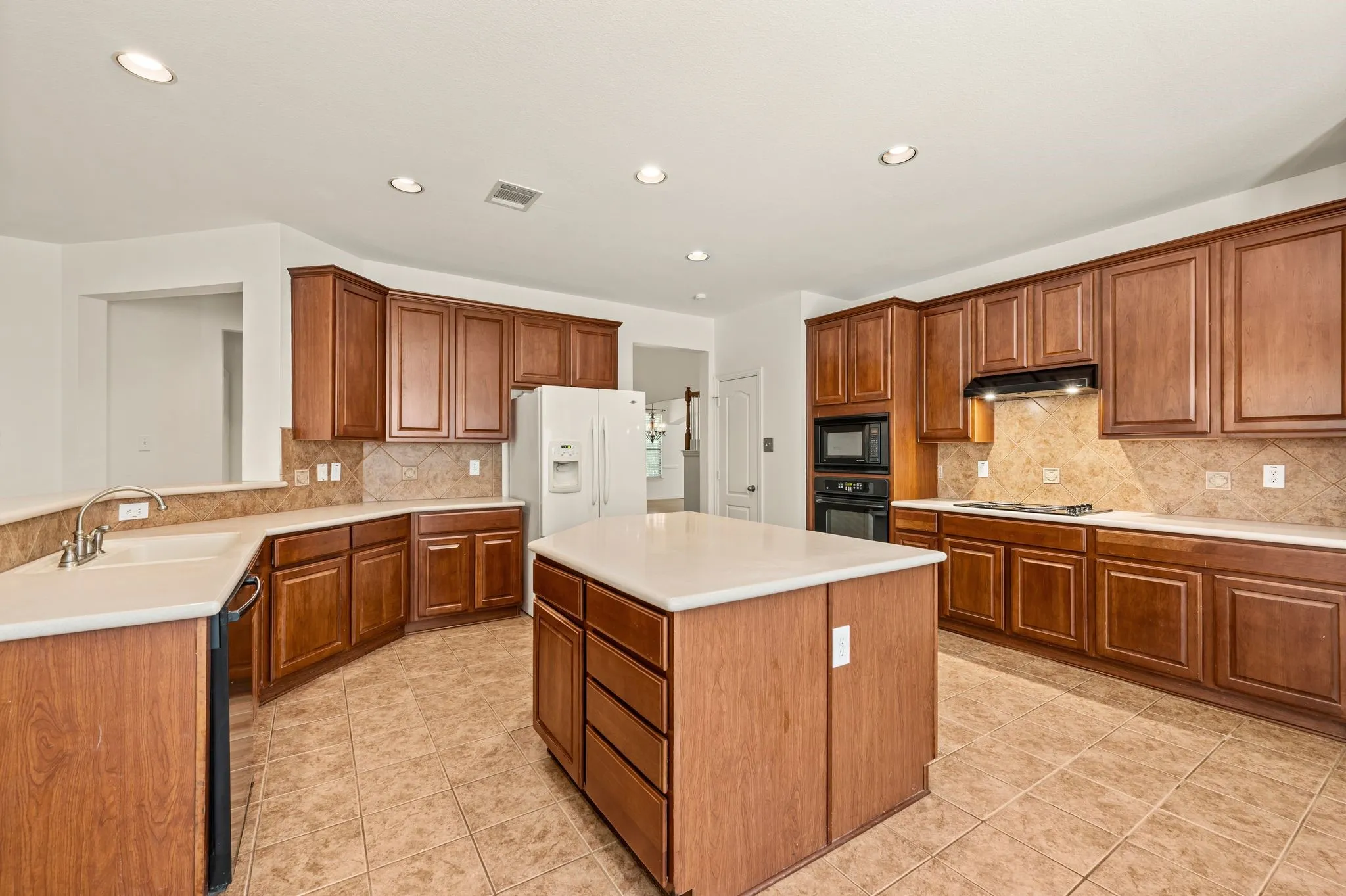 Spacious kitchen featuring warm wood cabinetry, neutral countertops, and a central island with storage