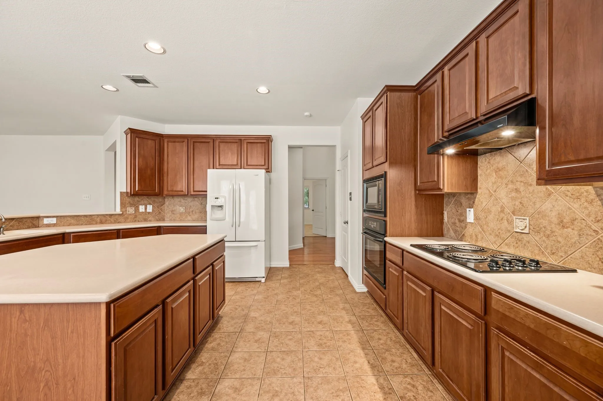 Spacious kitchen featuring warm wood cabinetry, light-toned countertops, and a full tile backsplash