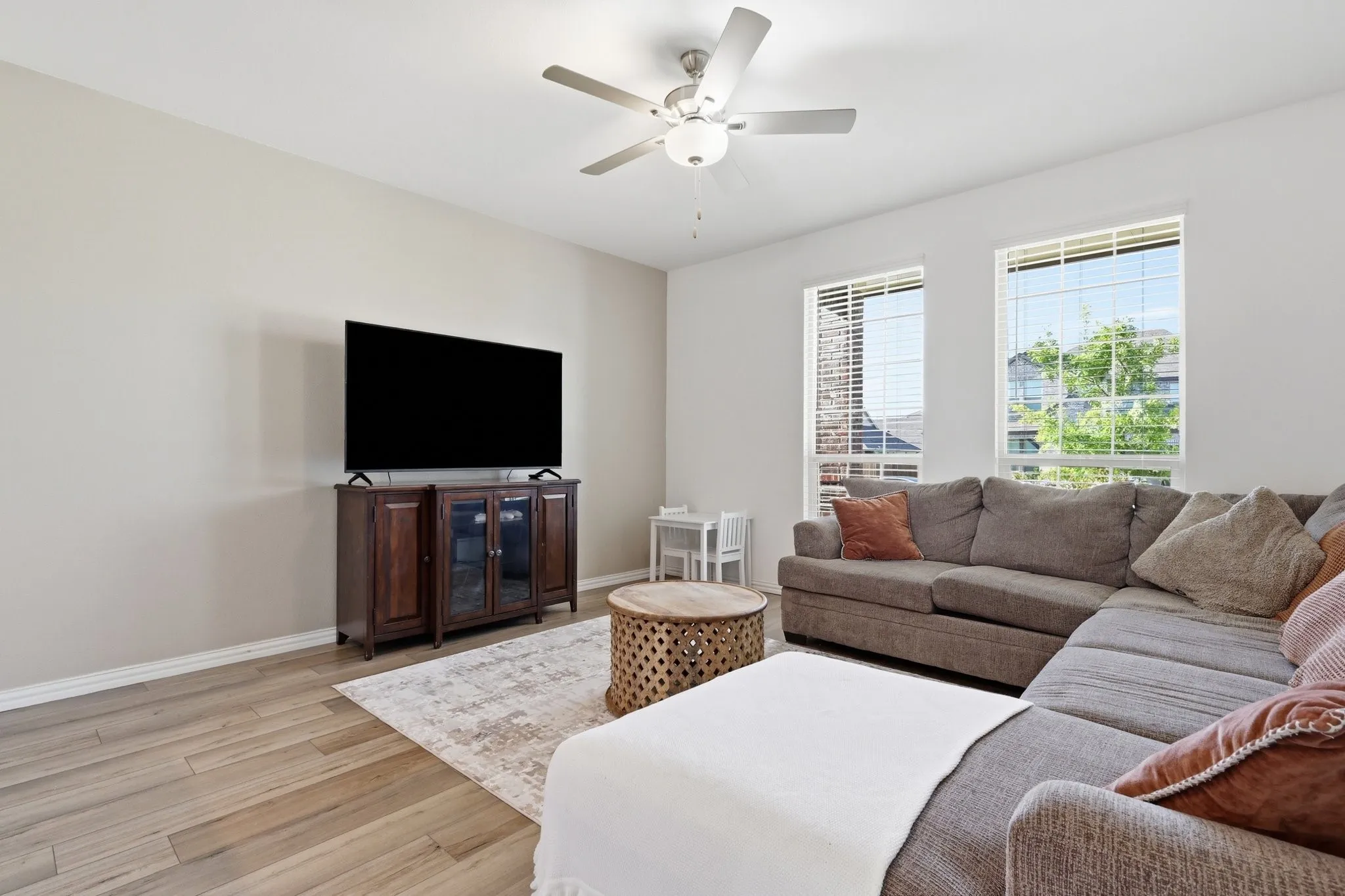 Light-filled living area featuring wood-finish flooring, neutral wall tones, and two large windows with blinds