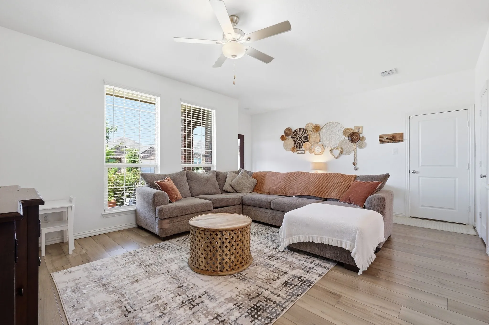 Open-concept living area featuring light wood-finish flooring, white walls, and a ceiling fan with integrated lighting