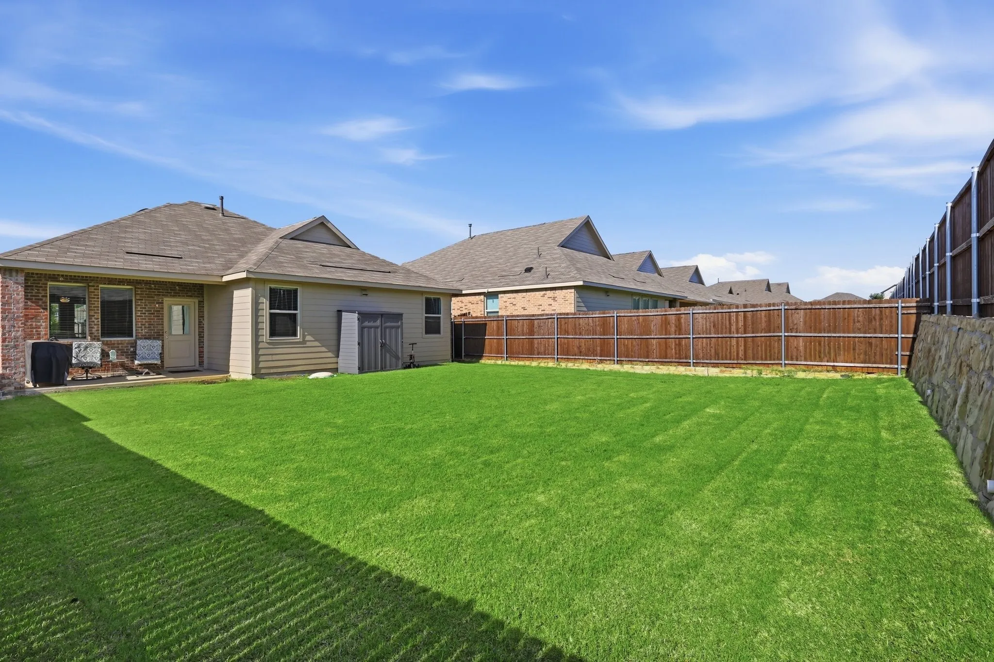 Expansive backyard featuring a manicured lawn, full privacy fencing, and a stone retaining wall