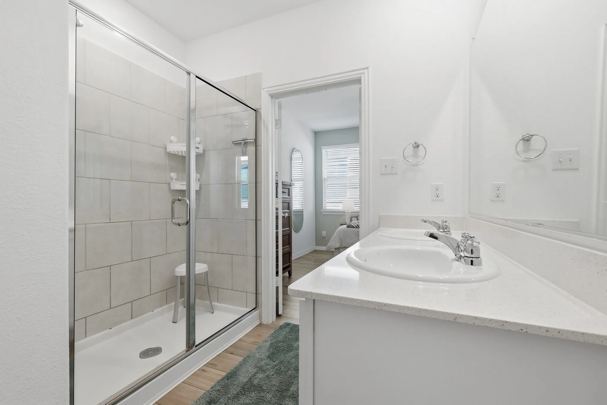 Spacious bathroom featuring a glass-enclosed shower with subway-style wall tile, a double vanity with an integrated countertop, chrome fixtures, and wood-finish flooring