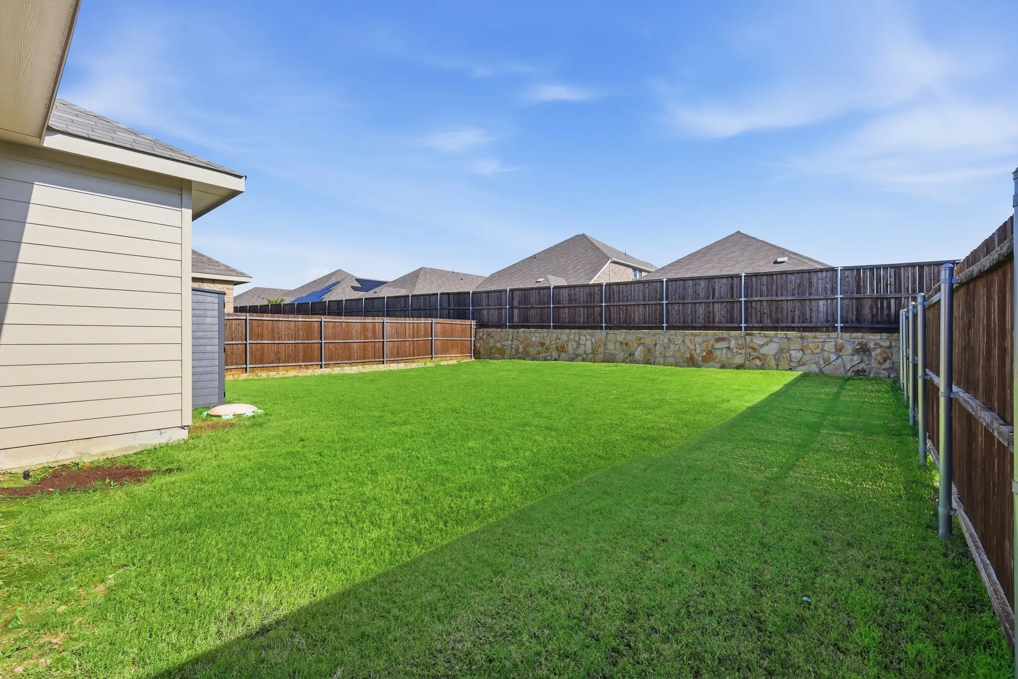 Expansive backyard featuring a manicured lawn, a full wood privacy fence, and a stone retaining wall