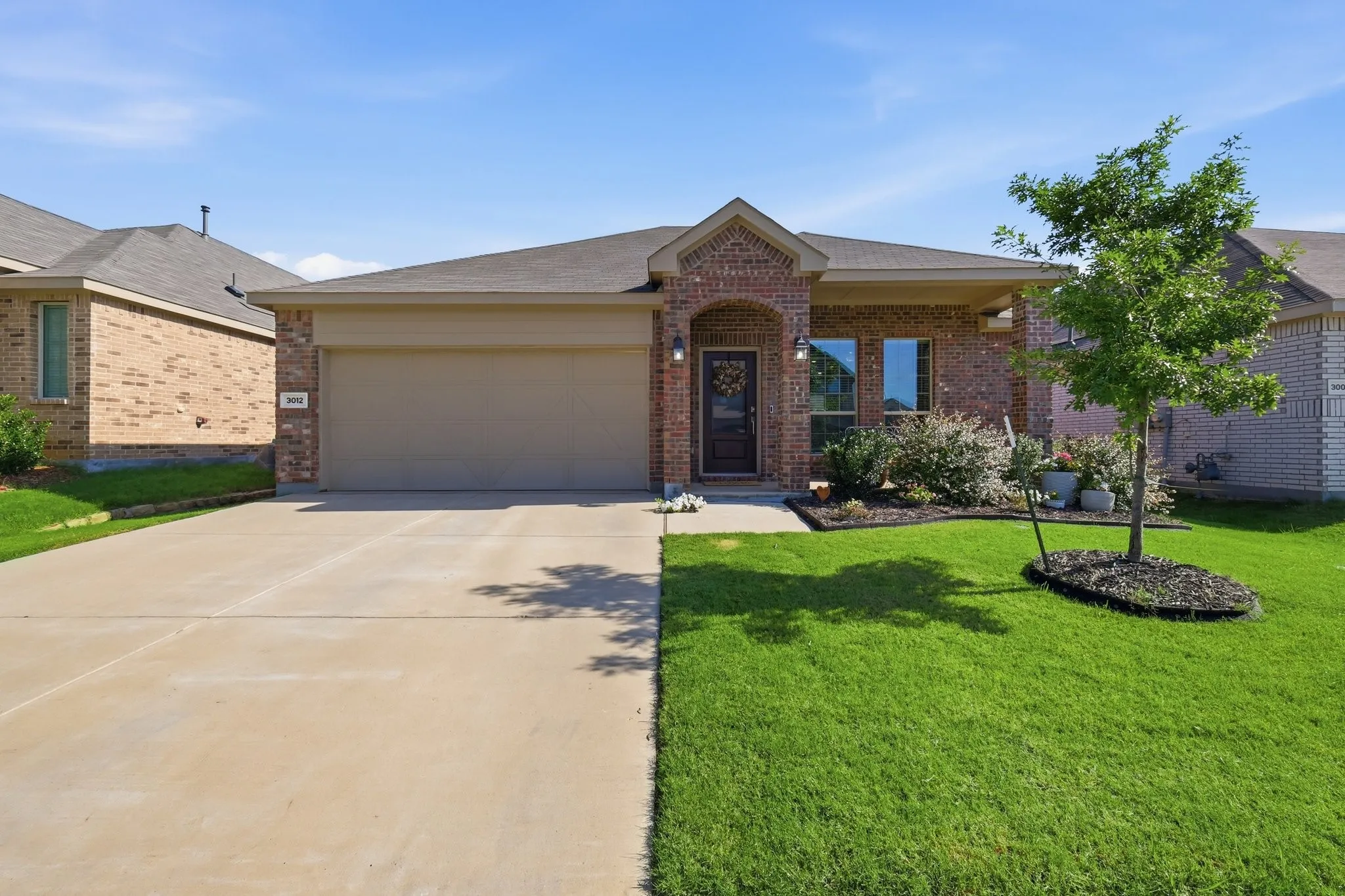 Brick facade home with an attached garage, covered entry, and a manicured lawn