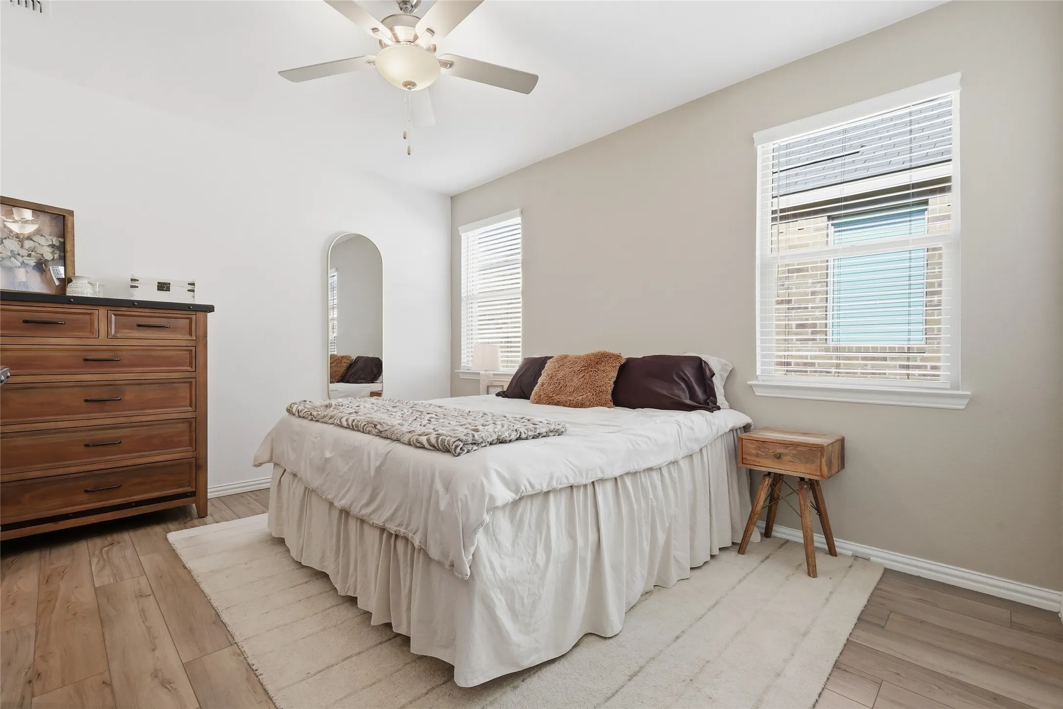 Spacious room featuring wood-finish flooring, two windows with blinds, a ceiling fan with integrated lighting, and neutral wall tones
