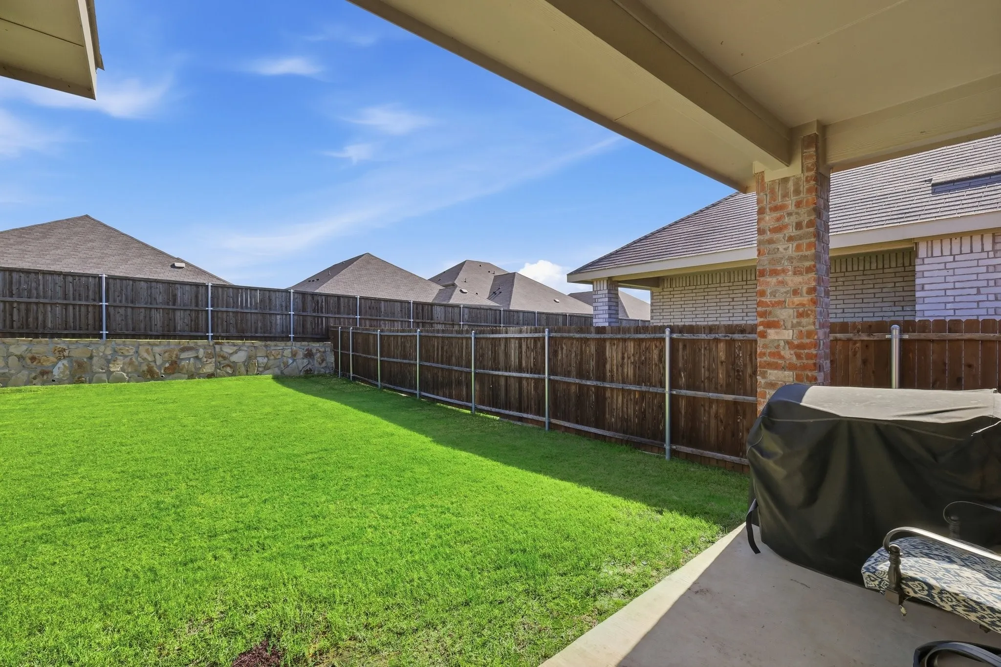 Expansive backyard with a manicured lawn, full wood fencing, and a stone retaining wall