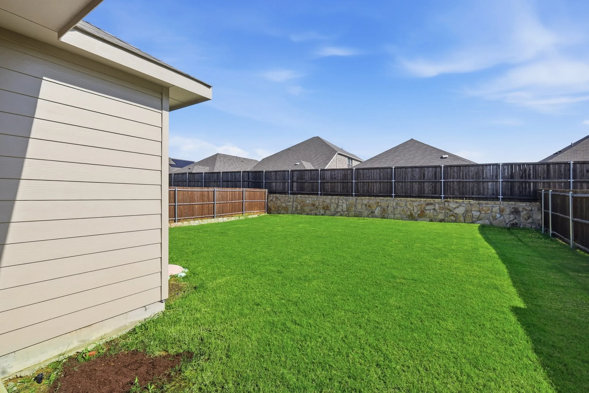 Expansive backyard featuring a manicured lawn, full privacy fencing, and stone retaining wall