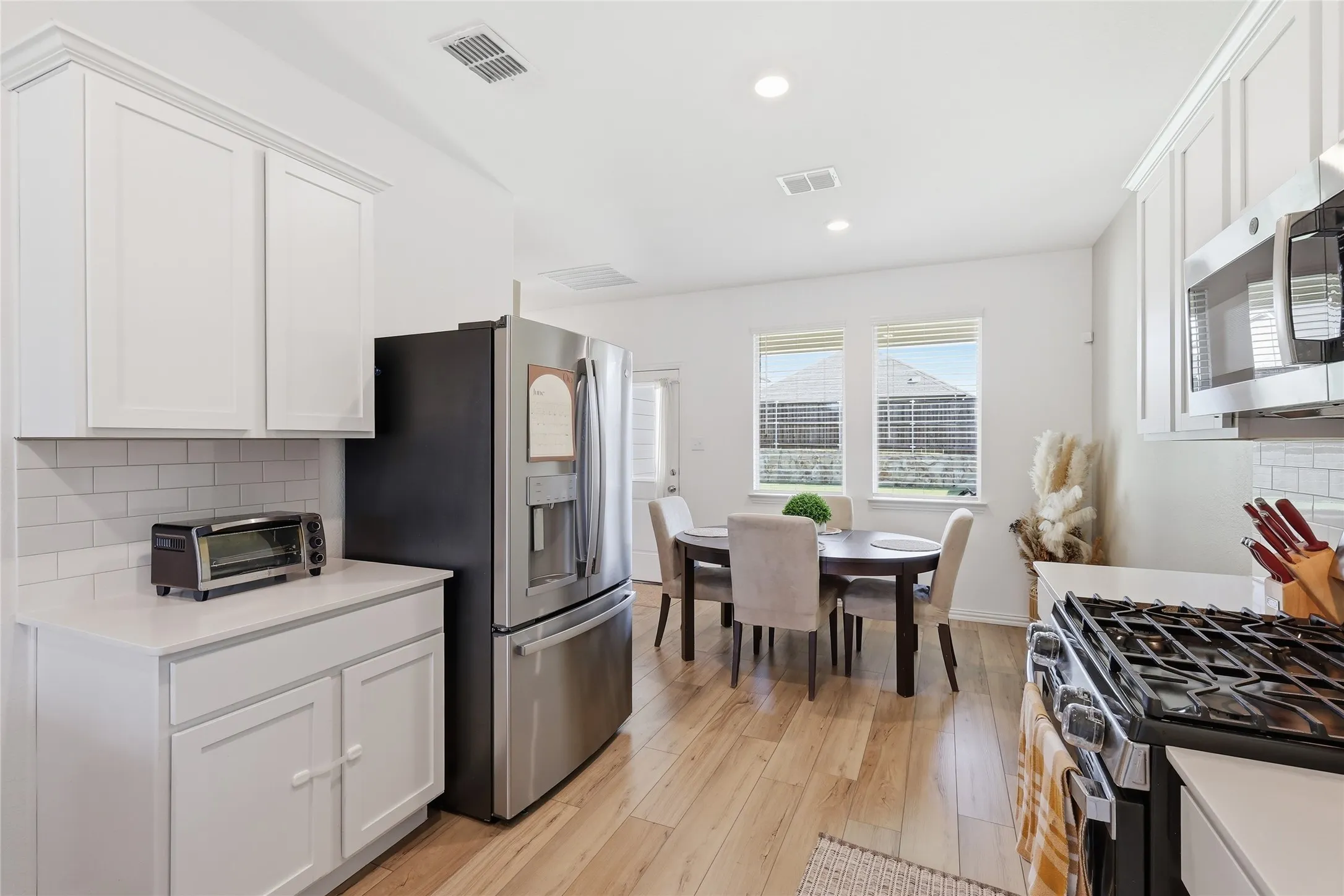 Modern kitchen featuring white cabinetry, light countertops, wood-finish flooring, a stainless steel refrigerator, and a built-in microwave