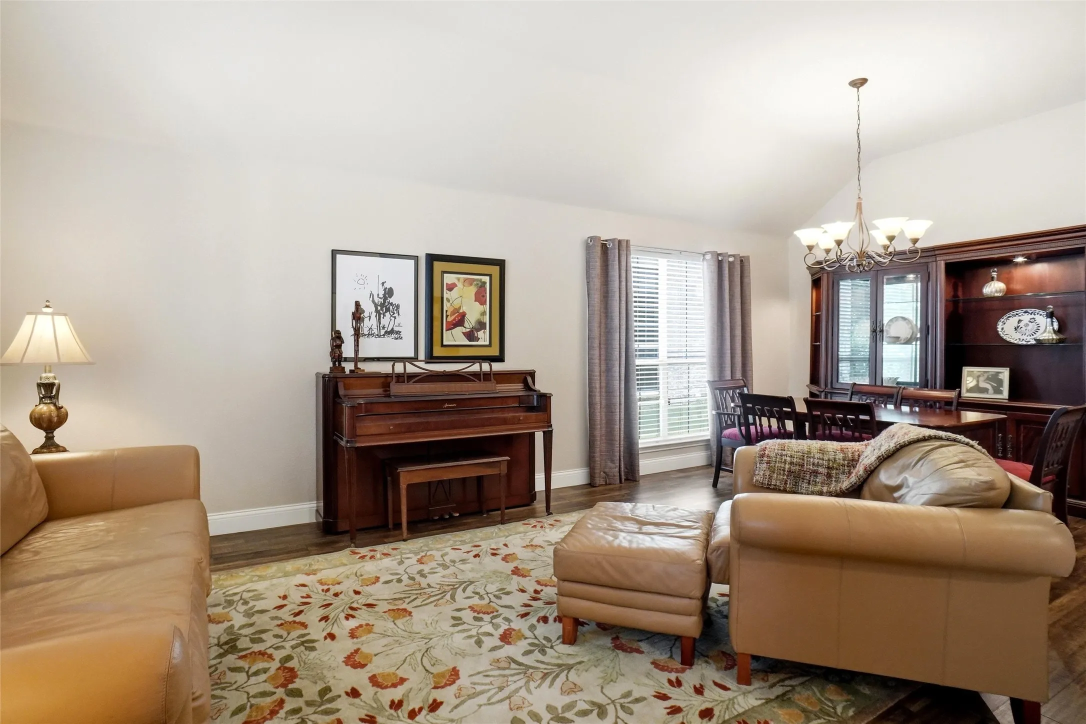 Spacious living area featuring vaulted ceilings, wood-finish flooring, and a large window with privacy blinds