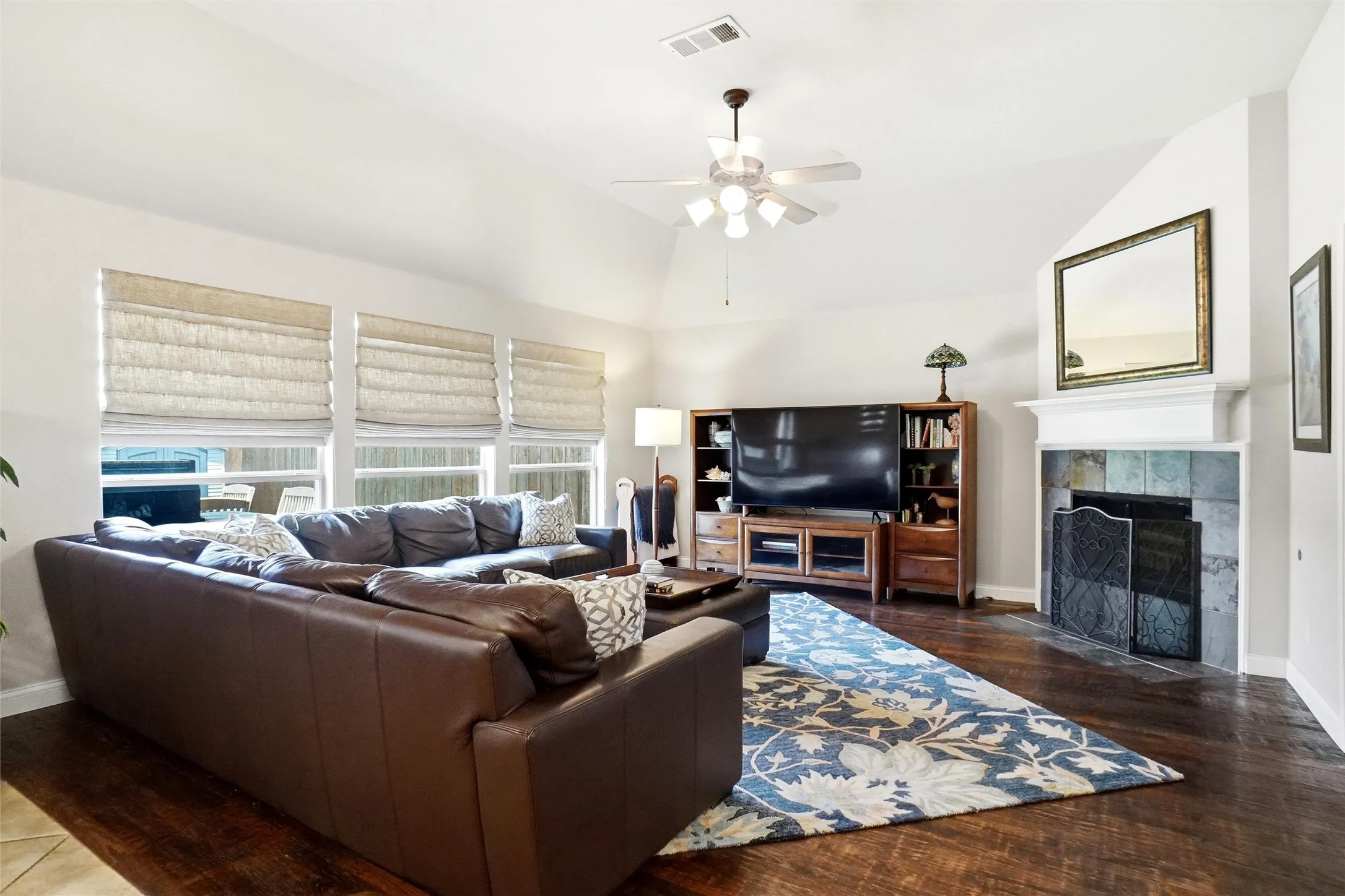 Living area featuring vaulted ceilings, wood-finish flooring, and a fireplace with a stone surround