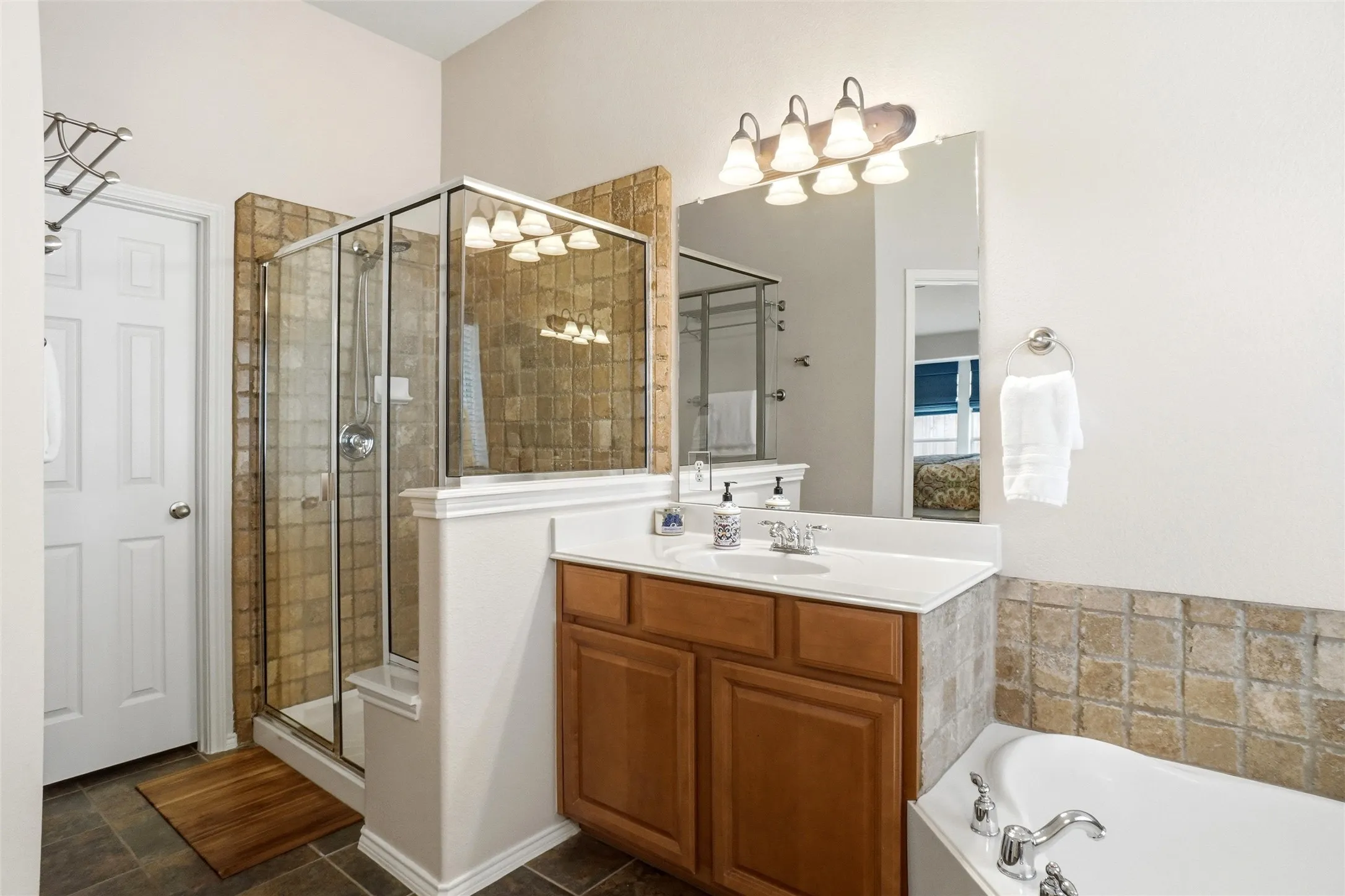 Bathroom featuring a glass-enclosed shower with tile surround, a single vanity with wood cabinetry and a white countertop, and a built-in bathtub with a tiled facade