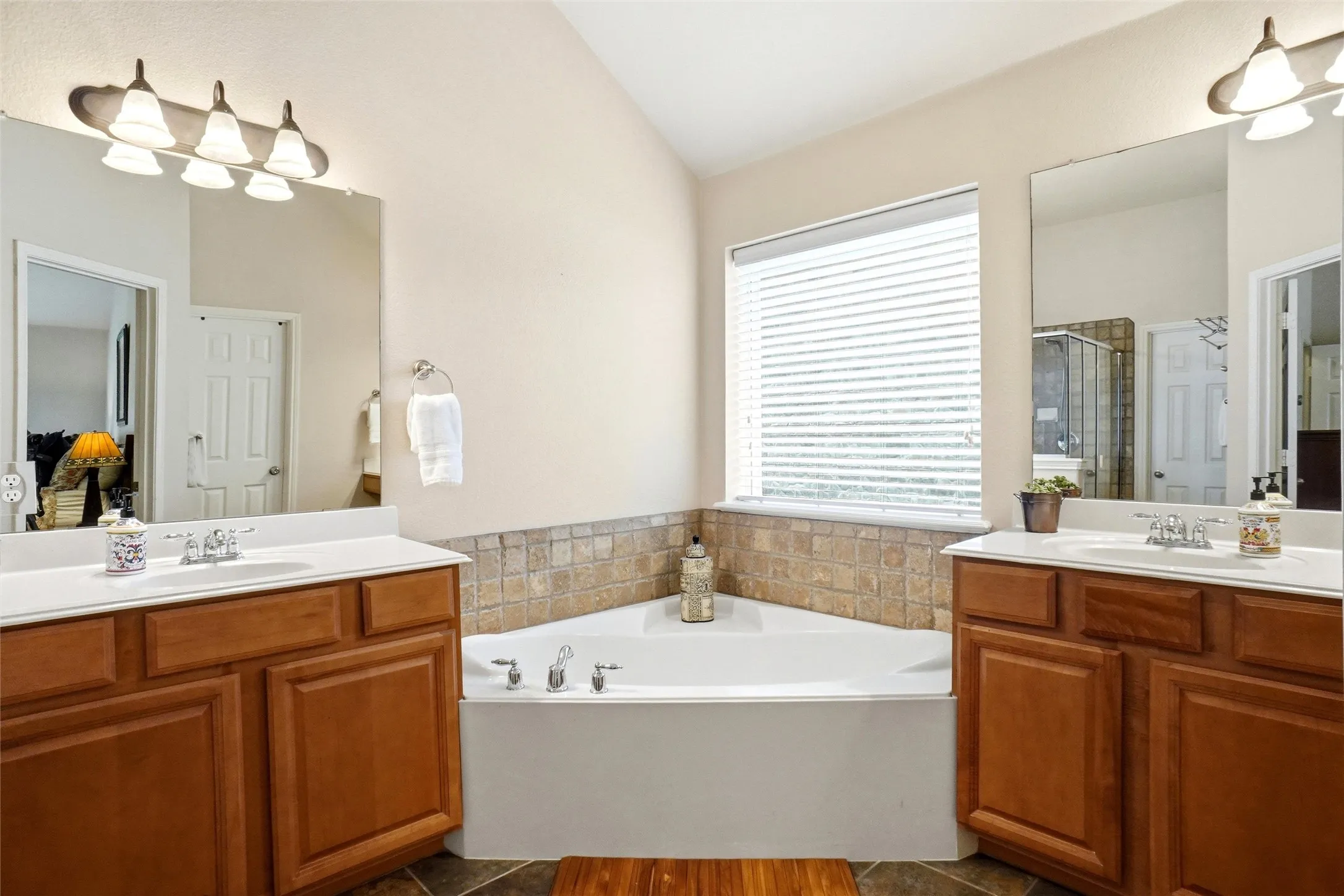 Corner soaking tub with a tiled surround, framed by two wood-finish vanities with undermount sinks and individual mirrors