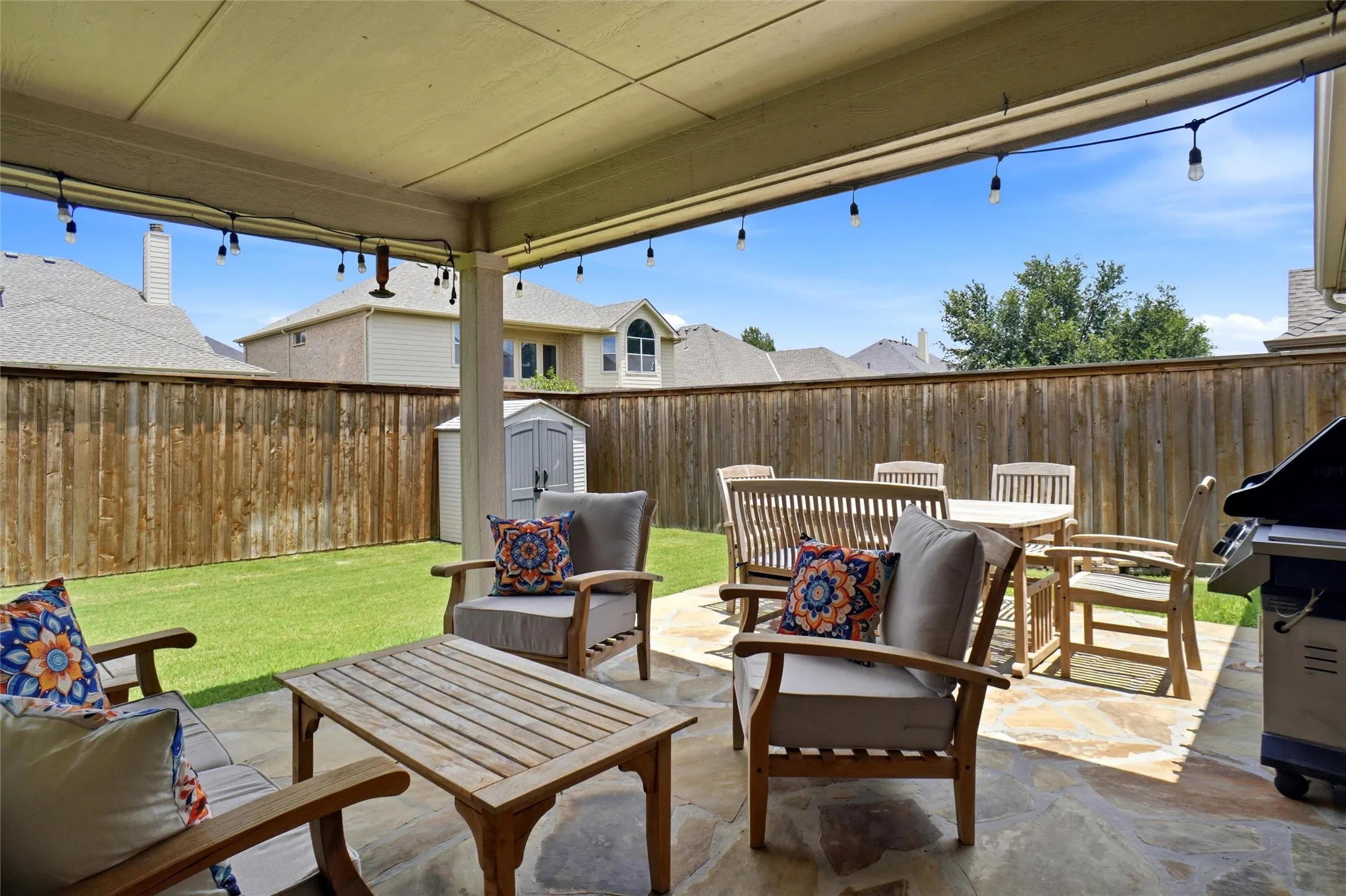 Expansive covered patio featuring flagstone flooring and direct access to a fenced backyard with a manicured lawn