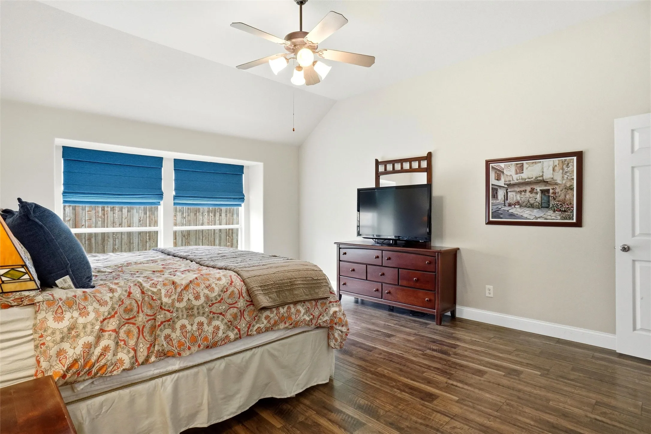 Vaulted ceiling room featuring wood-finish flooring, a ceiling fan with integrated lighting, and dual windows with blue Roman shades