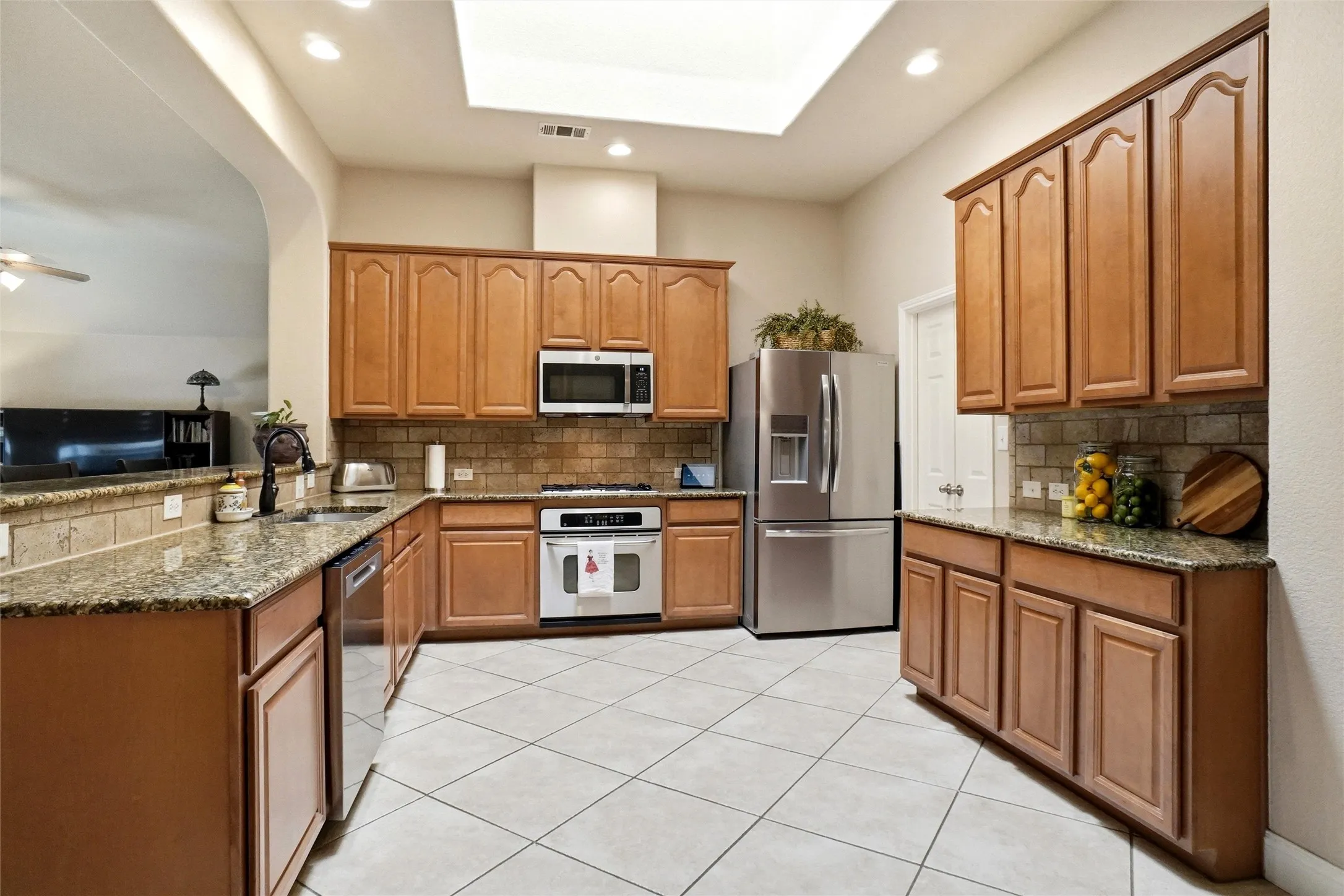 Kitchen featuring diagonal tile flooring, granite countertops, wood cabinetry, stainless steel appliances, and a skylight
