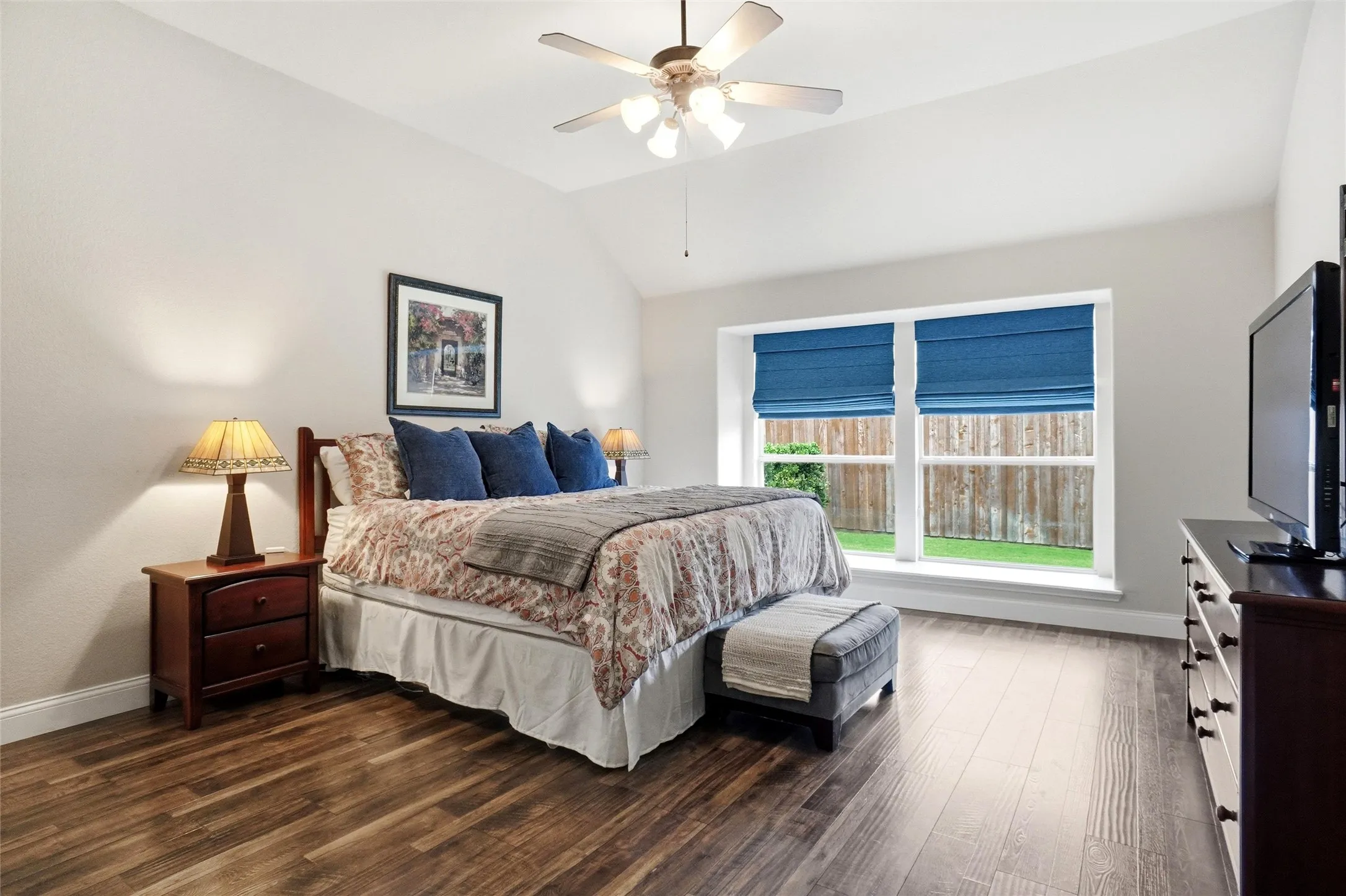Bedroom featuring a vaulted ceiling with a ceiling fan, wood-finish flooring, and a double window with blue Roman shades